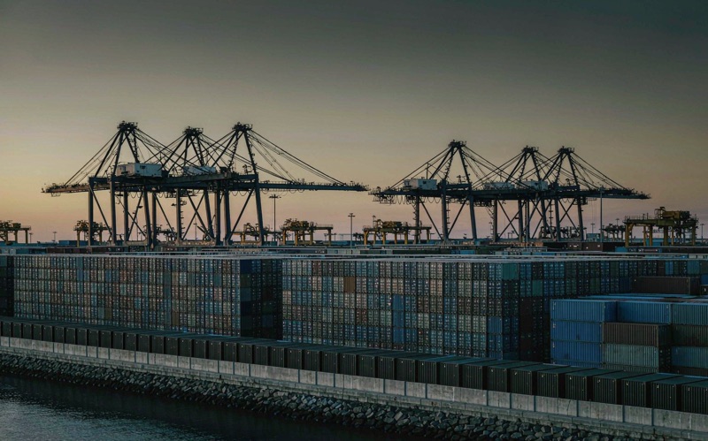 Container terminal at dusk with stacked boxes and silhouetted gantry cranes