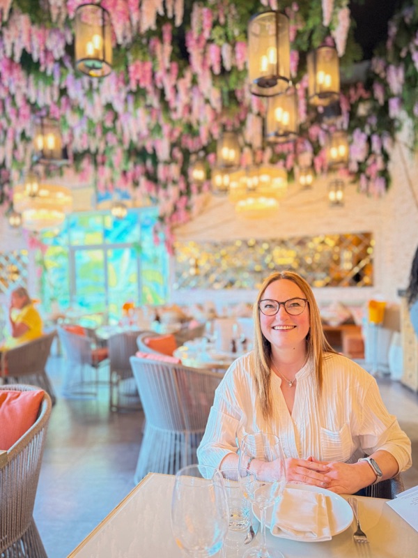 Mandy sitting at a table in Victor’s restaurant on the quayside, softly lit by natural daylight. She’s mid-laugh, relaxed but reflective, surrounded by elegant table settings and quiet ambience. The kind of moment that feels like a pause in the middle of a noisy world—small, beautiful, and real.