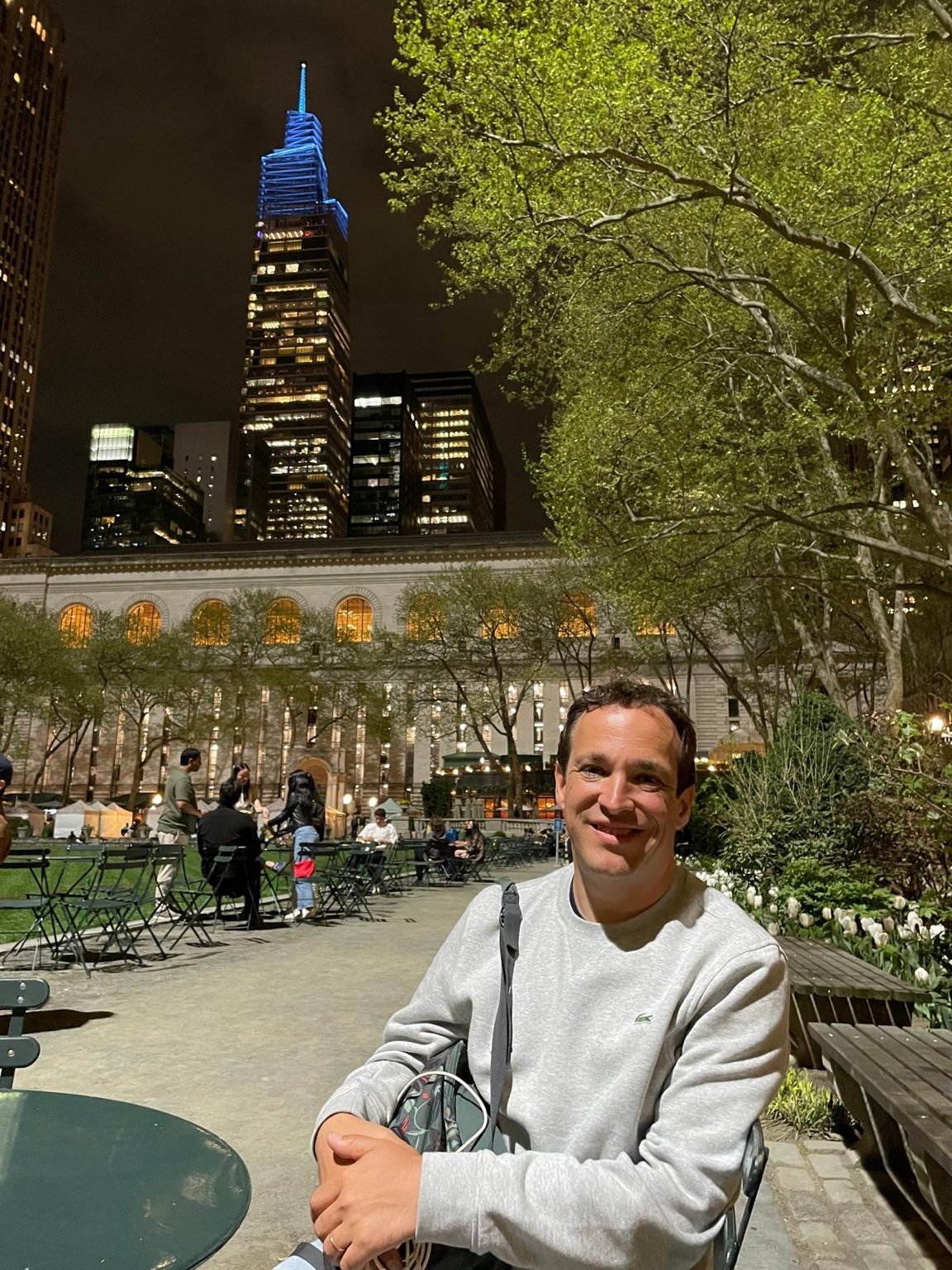 Mesas y sillas de Bryant Park de noche con rascacielos iluminados