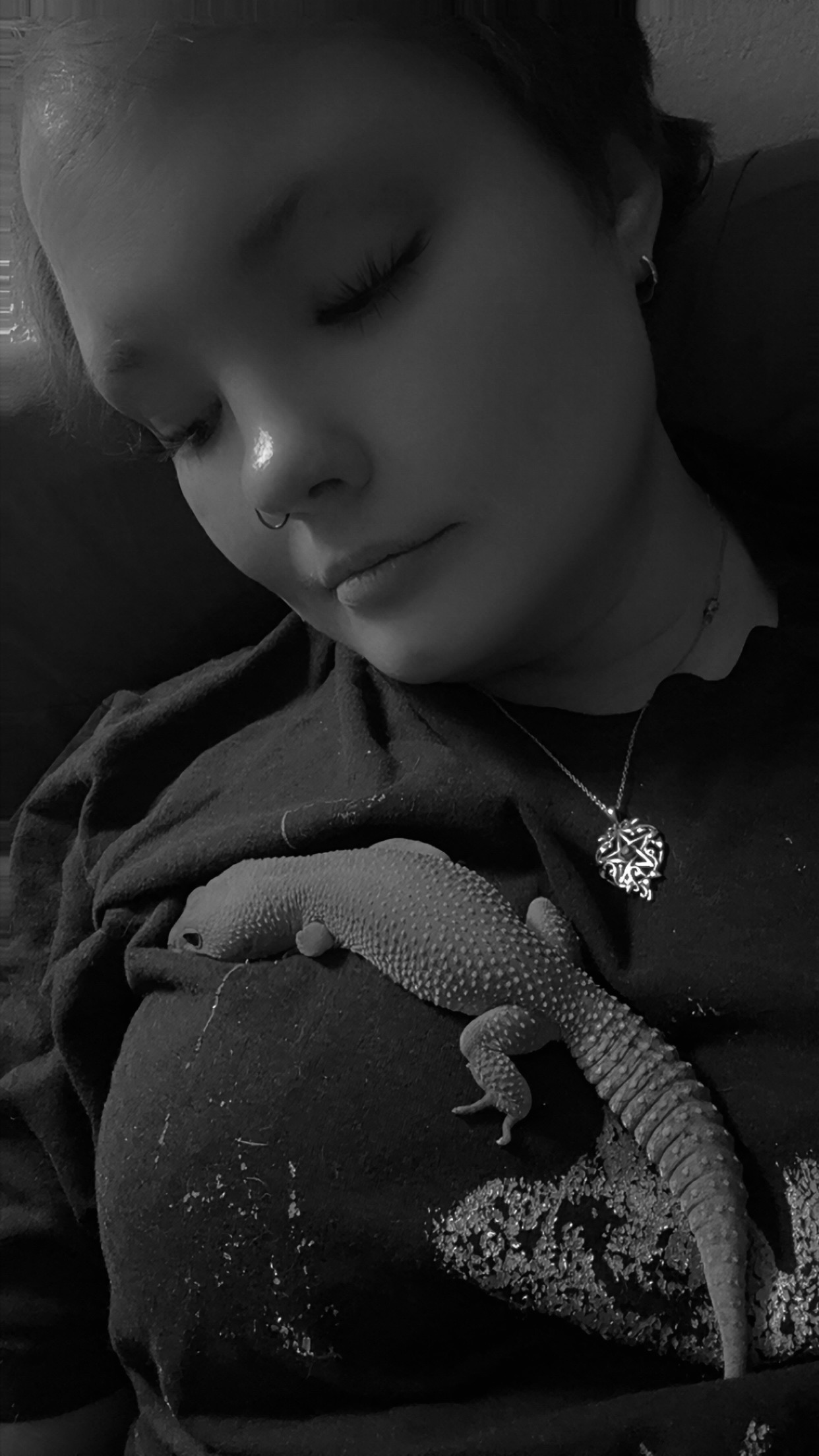 A black and white photograph of Ashley Randall looking down with a gentle, exhausted smile at her leopard gecko, Yennifer, resting on her chest during a POTS flare-up. A black and white photograph of Ashley Randall looking down with a gentle, exhausted smile at her leopard gecko, Yennifer, resting on her chest during a POTS flare-up.