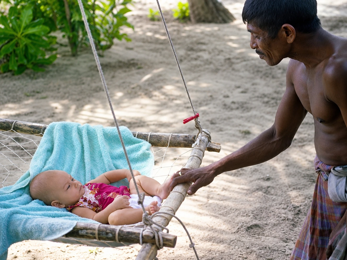 A man tending to a baby resting on a traditional rope swing/cot