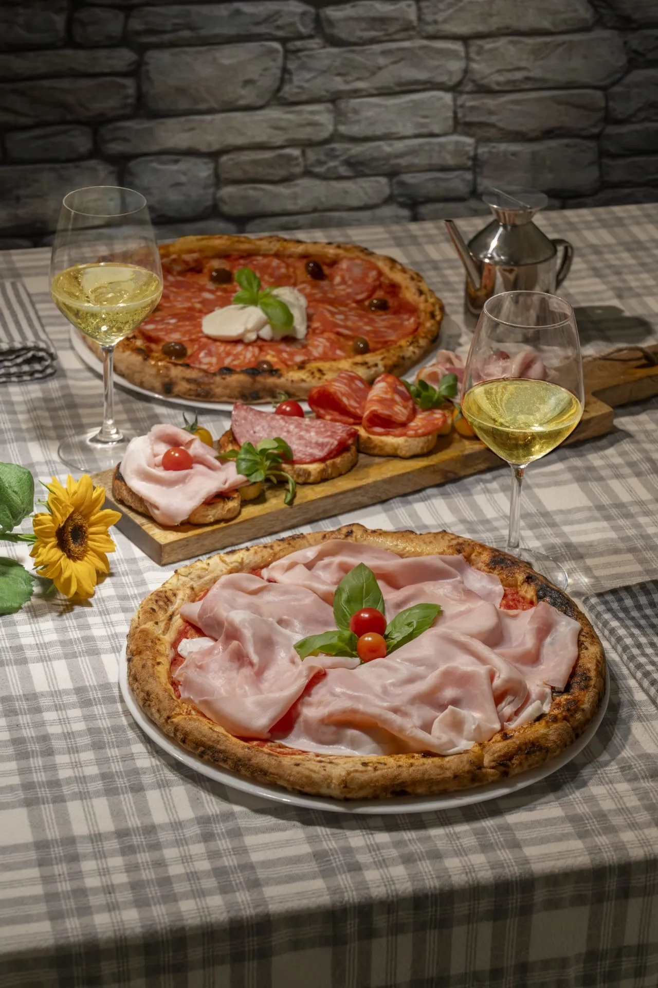 Tavolo che presenta due pizze farcite con prosciutto cotto e salame piccante. Al centro un tagliere con pane e salumi