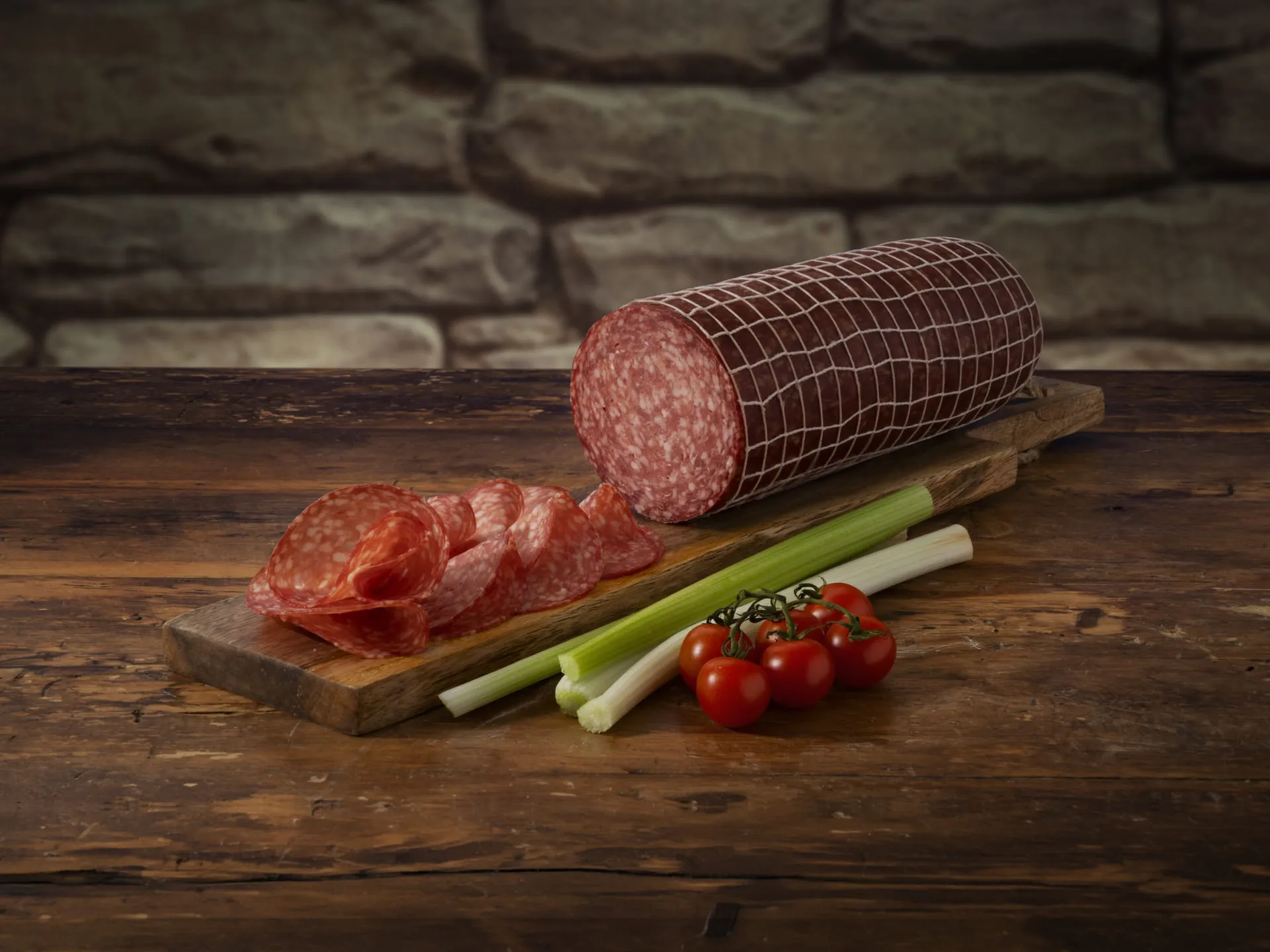 Salame Bombieri intero e a fette, accompagnato da pomodorini e sedano croccante, su un tagliere di legno