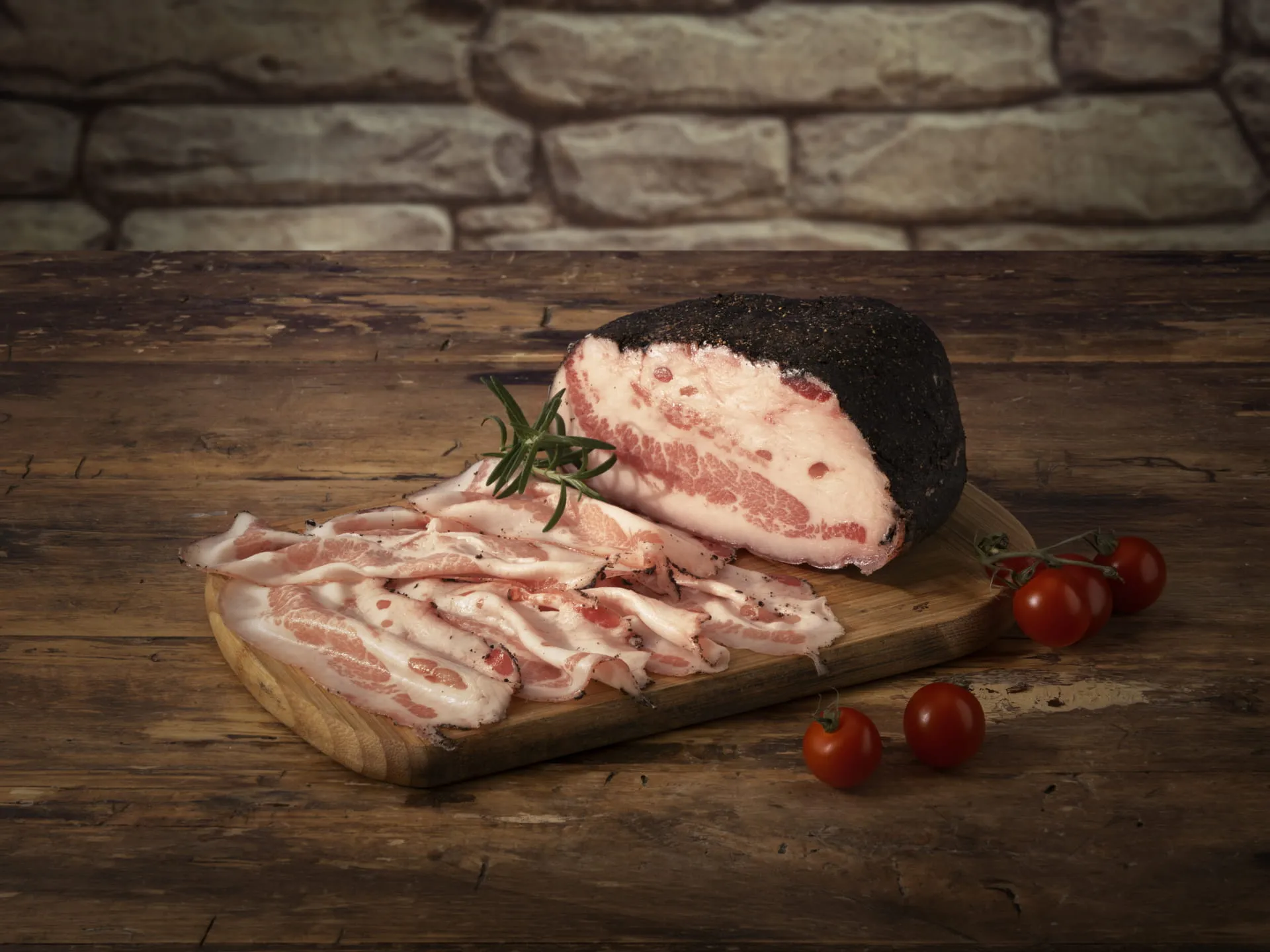 Bombieri aged and sliced Pancetta, with rosemary and cherry tomatoes, on a wooden cutting board