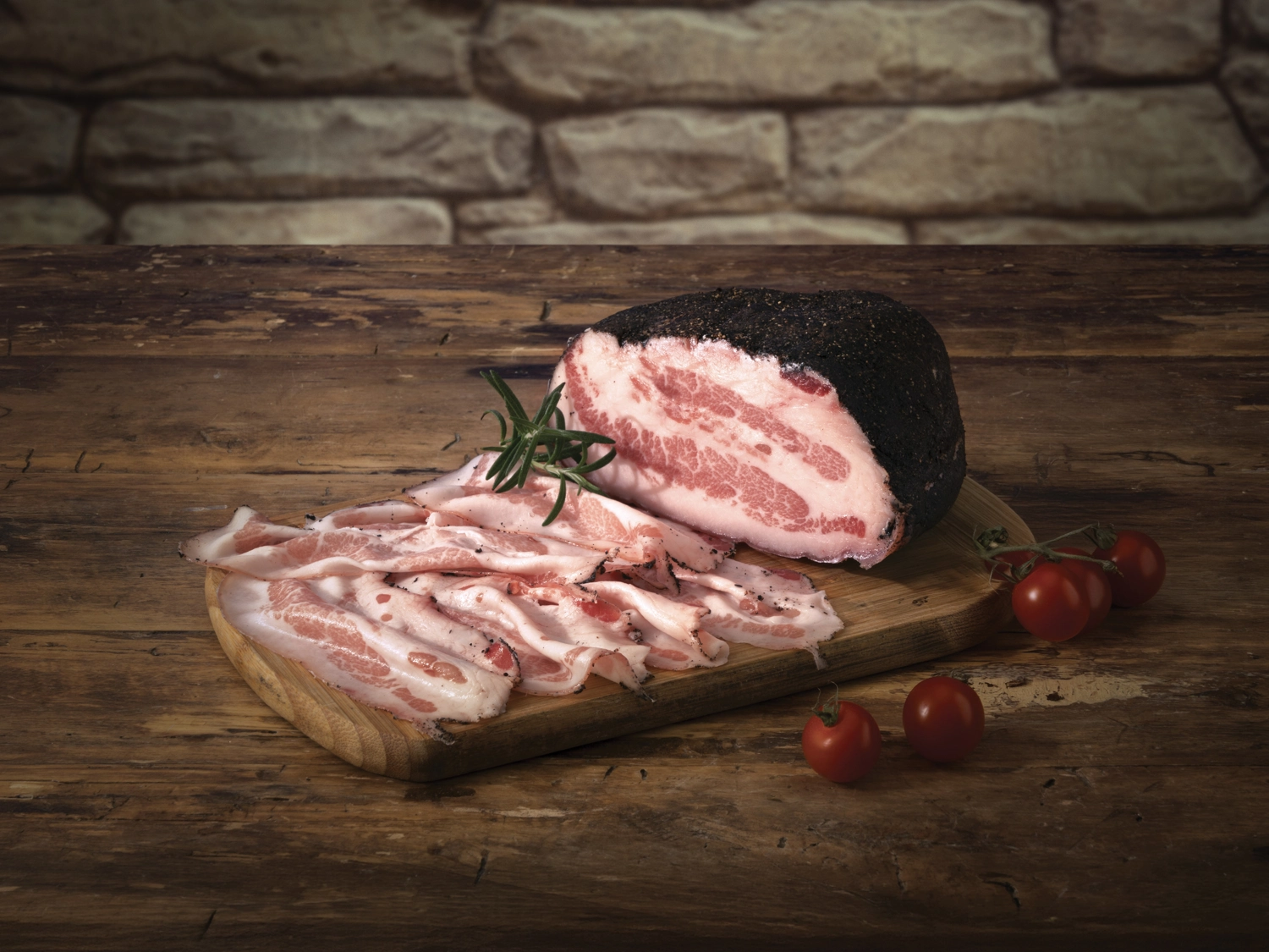 Pancetta Bombieri stagionata e affettata, con rosmarino e pomodorini, su tagliere di legno