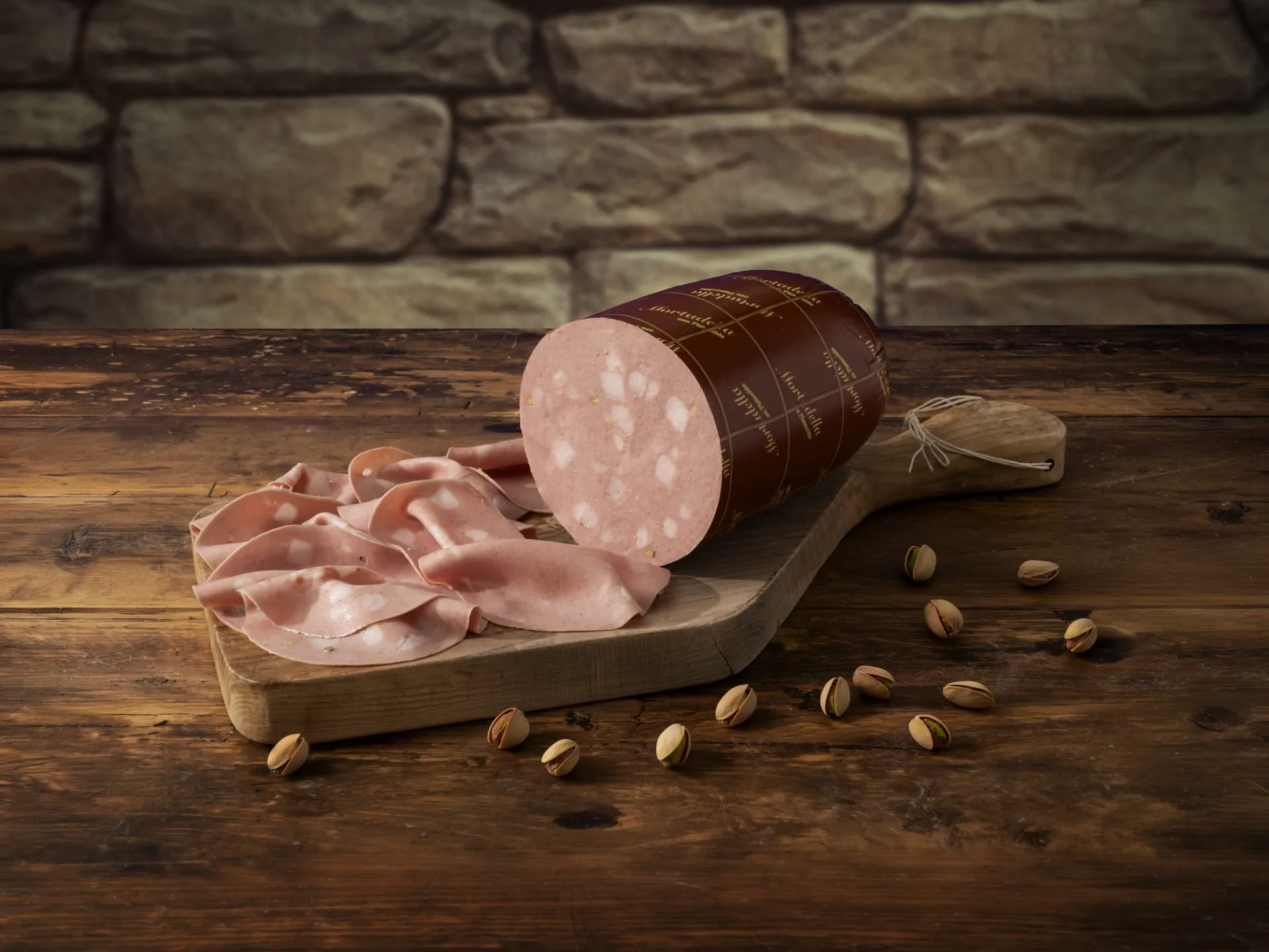 Mortadella Bomberi intera e affettata finemente su un tagliere. Di fianco pistacchi.