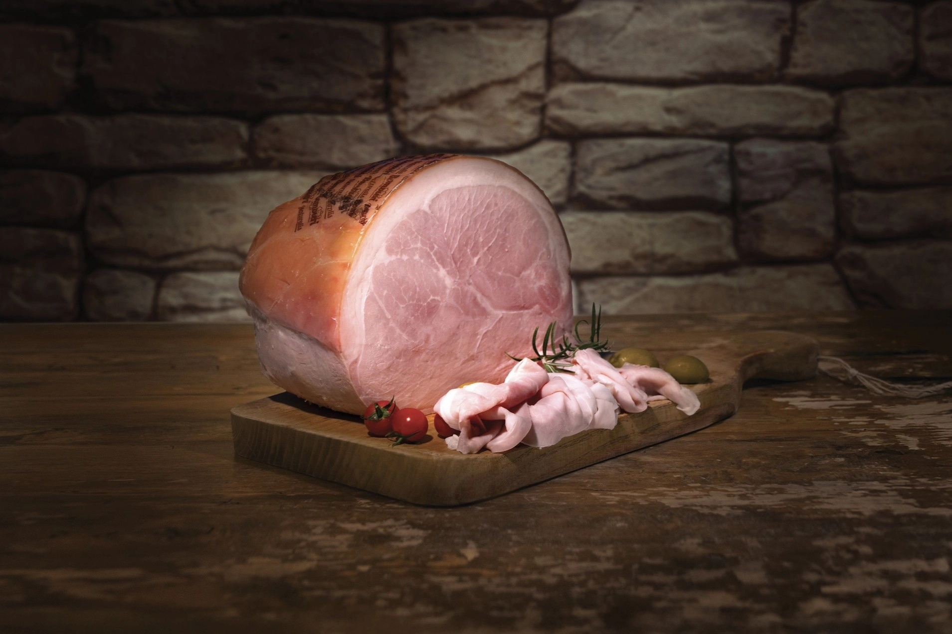 bombieri-prosciutti-cotti.webp Foto di un prosciutto cotto Bombieri disposto su un tagliere. Accanto il prosciutto affettato con pomodorini e olive
