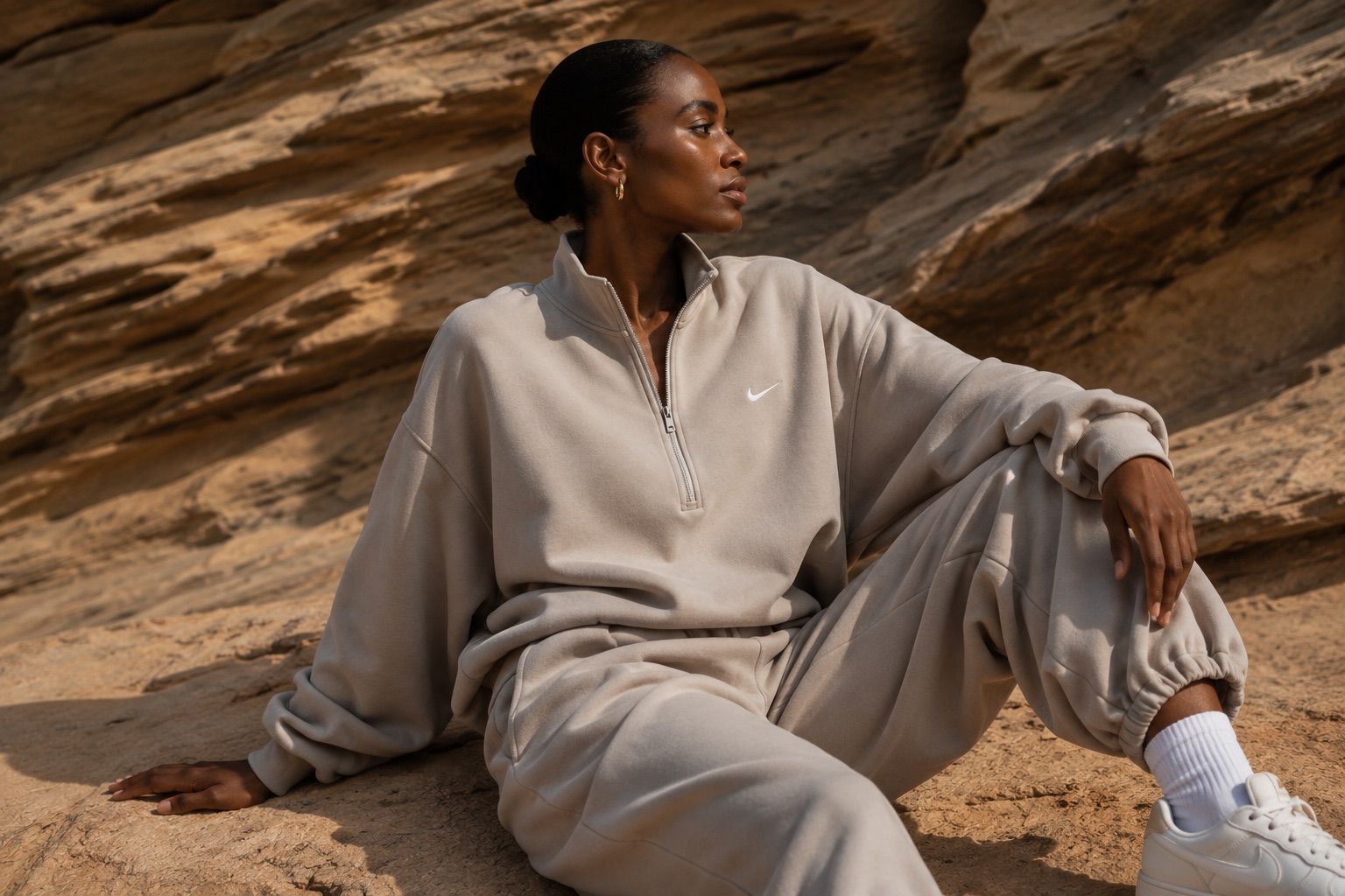 Woman wearing a neutral Nike tracksuit seated against sunlit rock formations