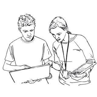 A student holds a laptop computer and shows something to their instructor. The instructor is holding a tablet and pointing at something on the student’s screen. 