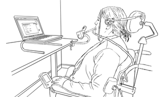 A person in a wheelchair with a sip and puff device using a laptop propped up on a stand.