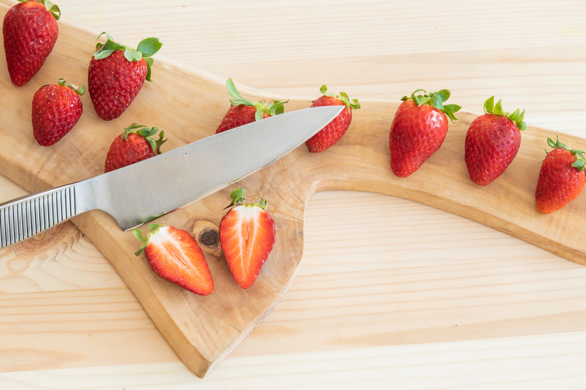 Fresh strawberries and grapes arranged on a light wooden board, soft daylight highlighting their colors