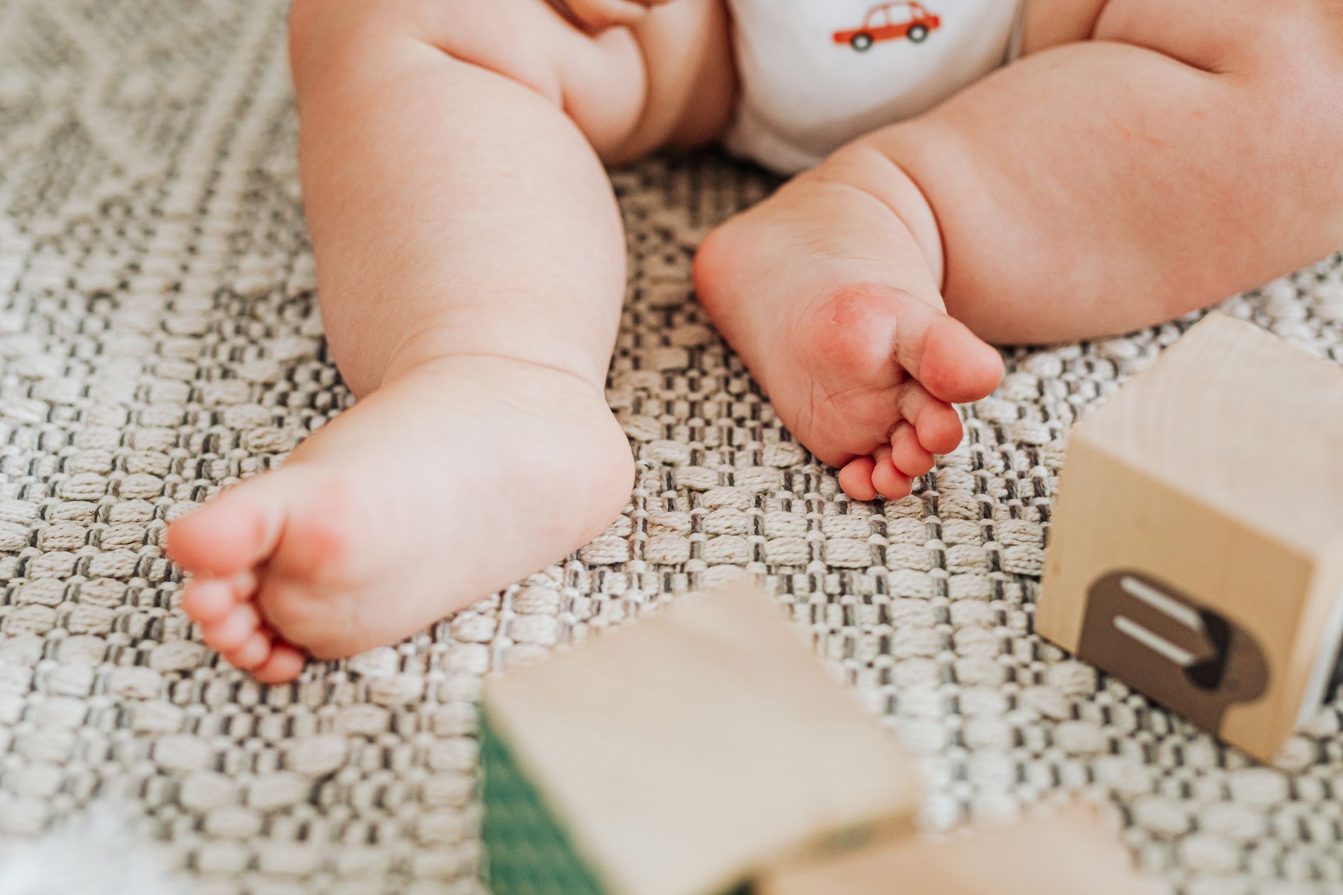 Happy six‑month‑old baby sitting on a soft rug, reaching for a colorful stack of silicone blocks, bright afternoon light