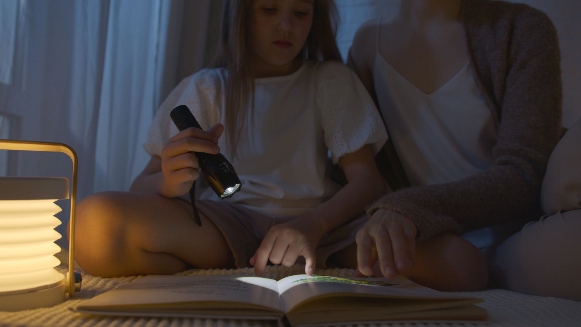 Parent reading to toddler by flashlight at night.
