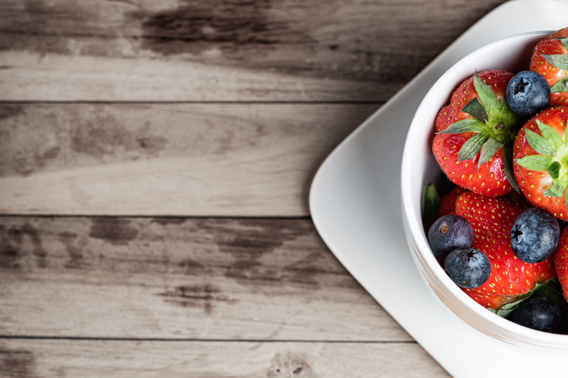 Close‑up of a pregnant woman's belly resting on a wooden board with a fresh fruit salad, bright natural light highlighting the curve
