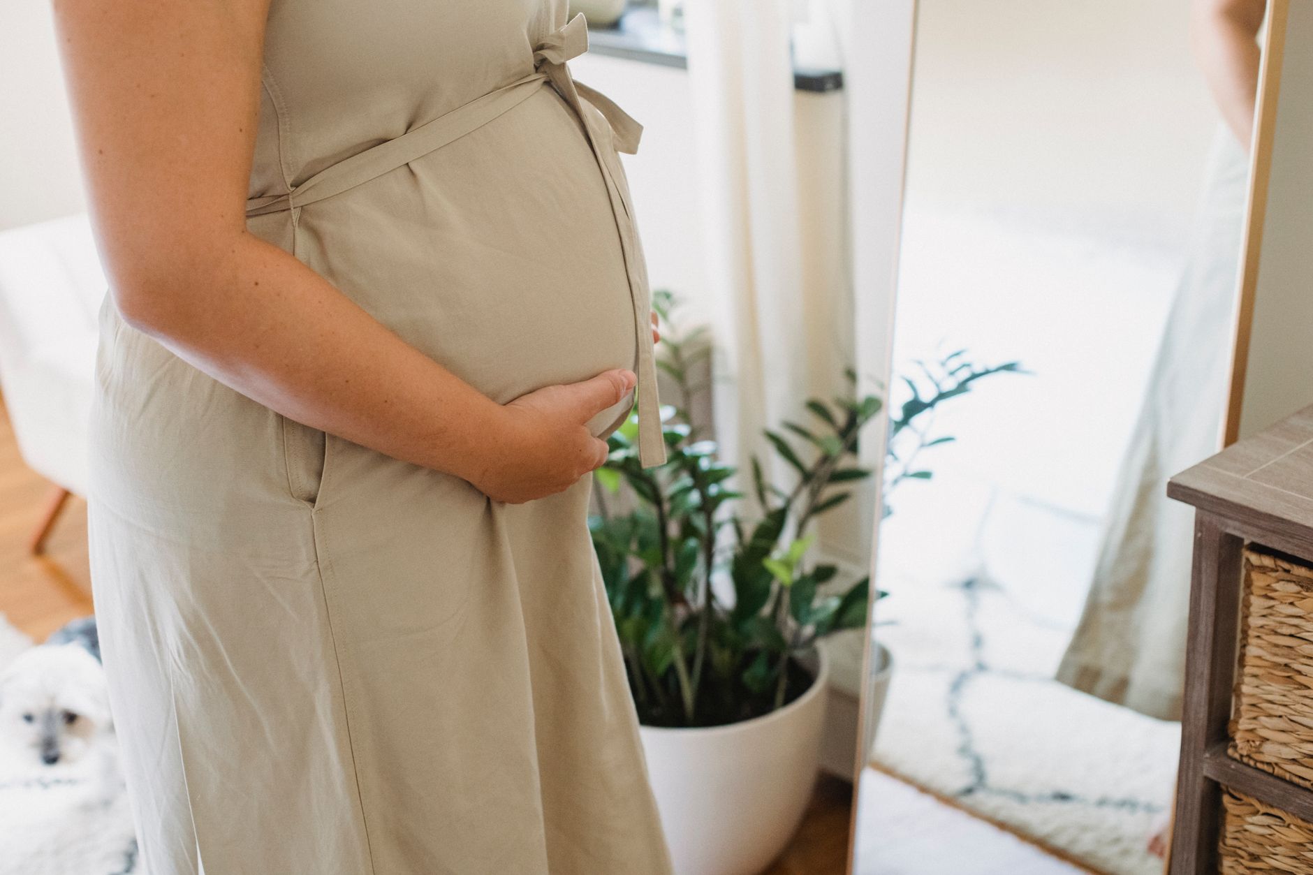 Pregnant woman standing in front of a mirror checking her posture, wearing a fitted maternity dress