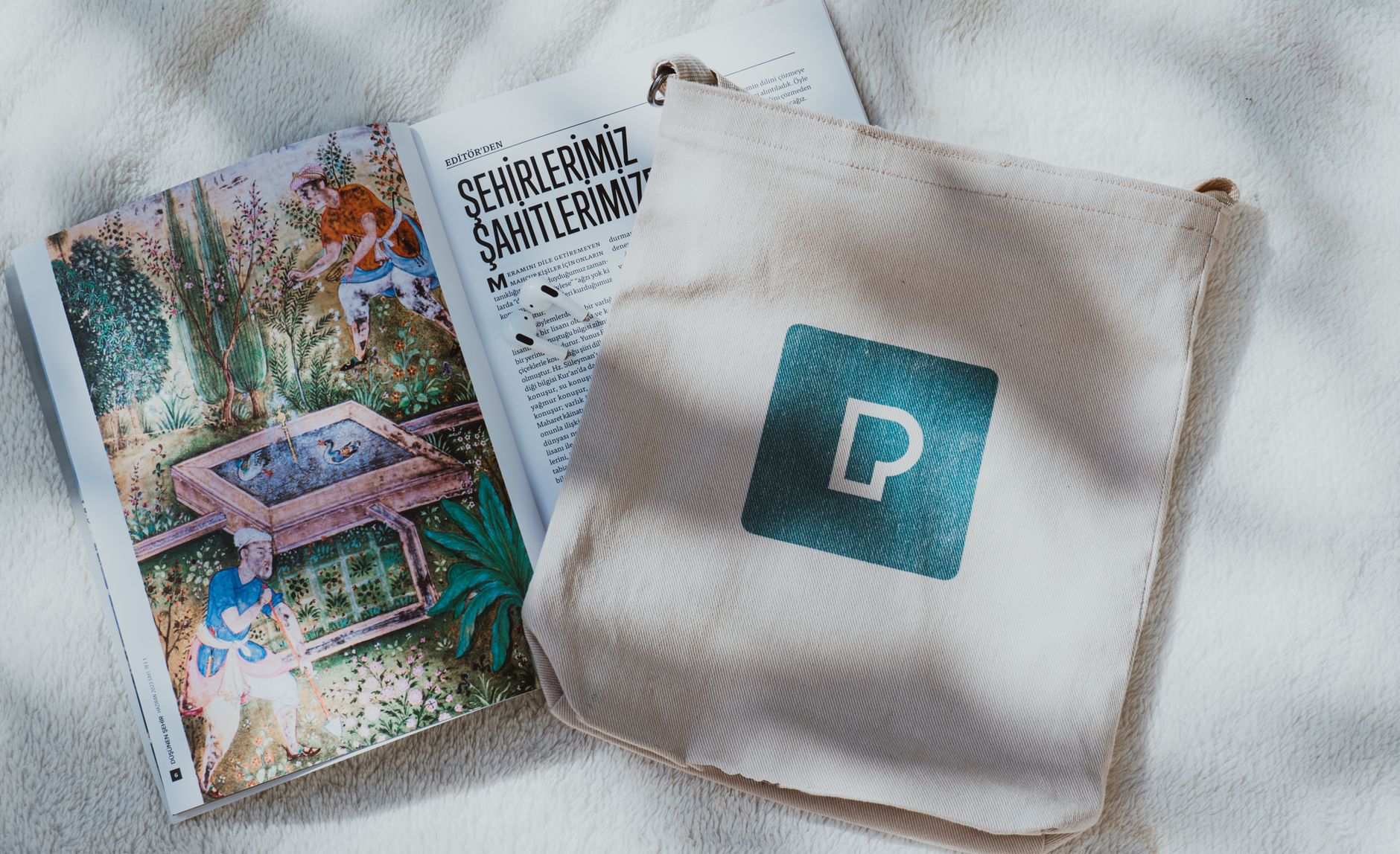 A soft, pastel-colored travel tote open on a bedside table, showing a water bottle, a prenatal vitamin bottle, and a folded pregnancy guide, natural morning light streaming in