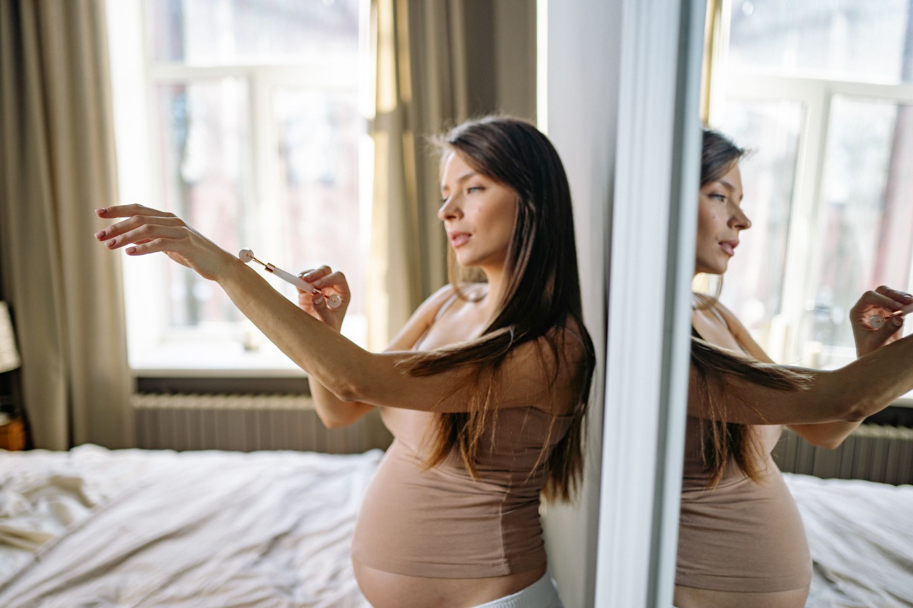 Pregnant woman looking at her belly in the mirror, soft natural light, showing the shape and size of her 24-week bump