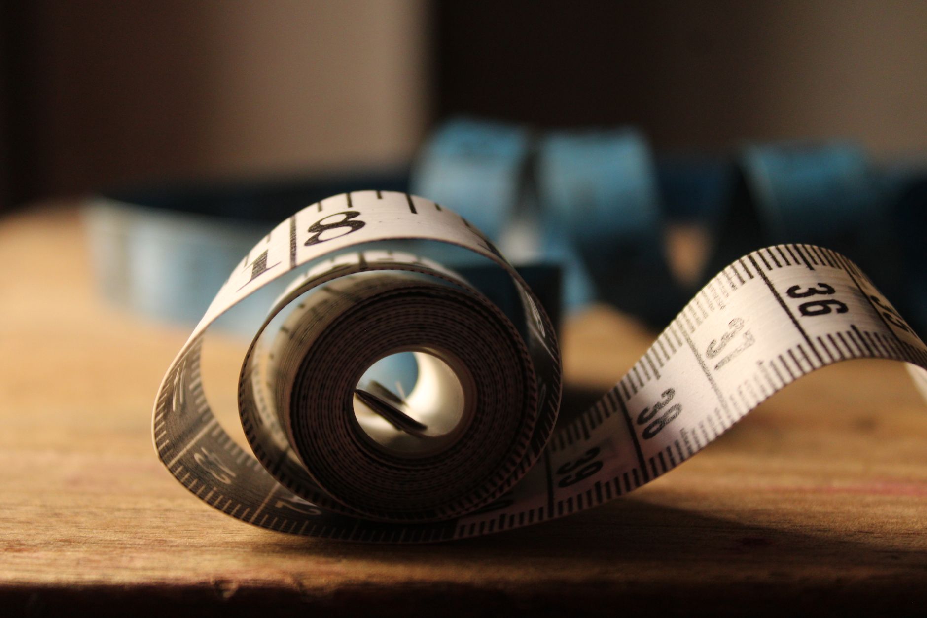 Close‑up of a flexible measuring tape laid across a pregnant belly, soft natural light, minimal background, clear numbers in inches and centimeters