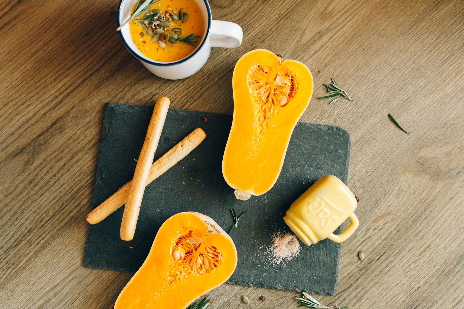 A ripe mango, a head of cauliflower, and a small butternut squash arranged on a wooden board