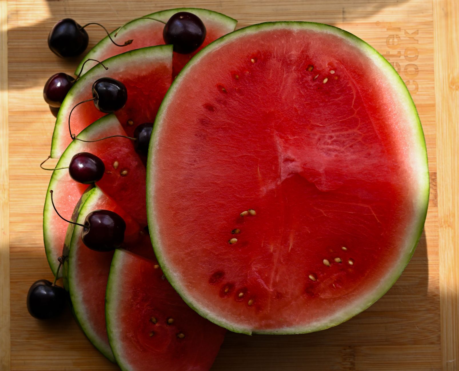 A small seedless watermelon next to a large slice of watermelon on a wooden board
