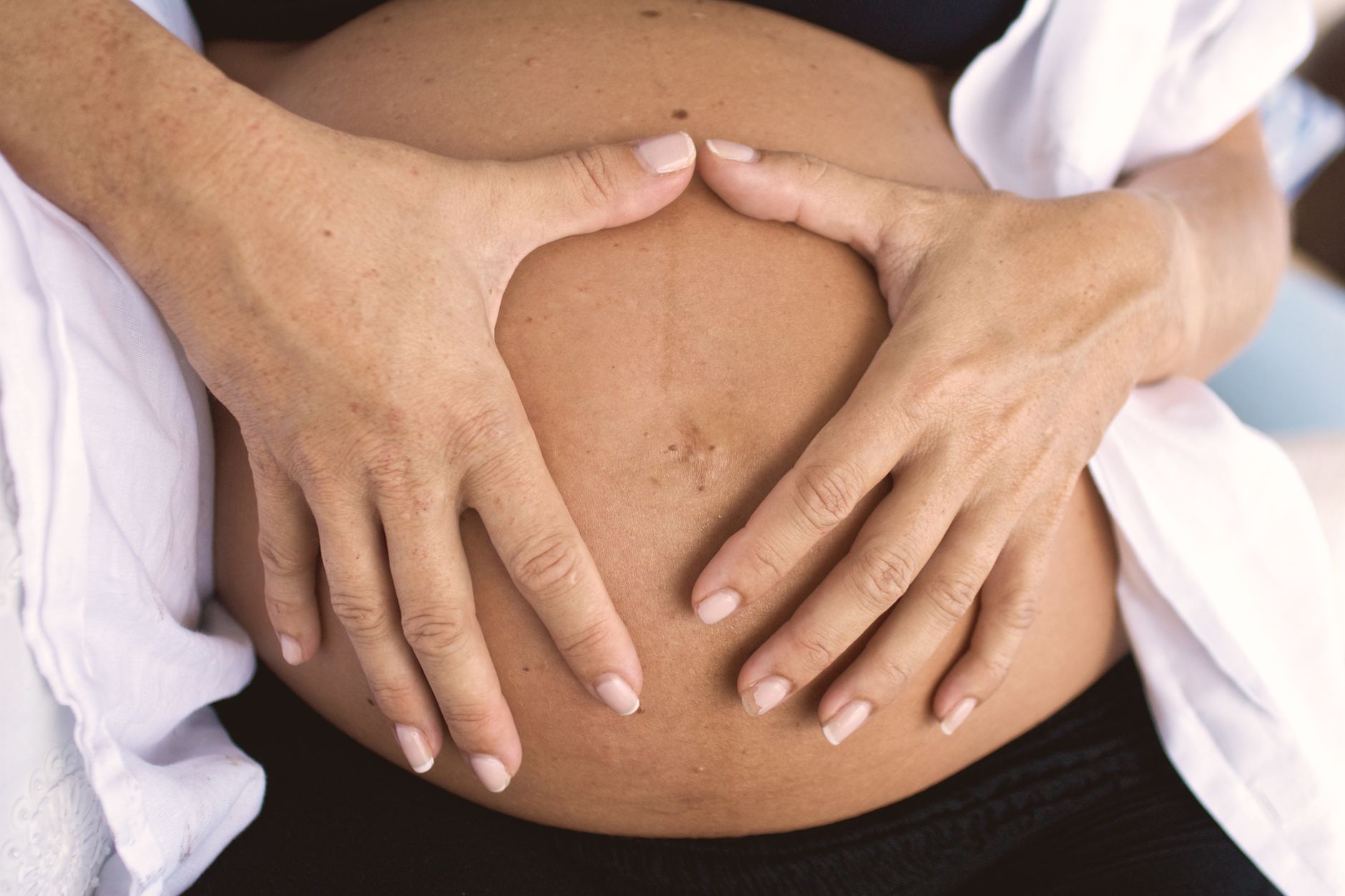 A close‑up of a pregnant woman's hand gently resting on a soft belly, warm natural light highlighting the skin