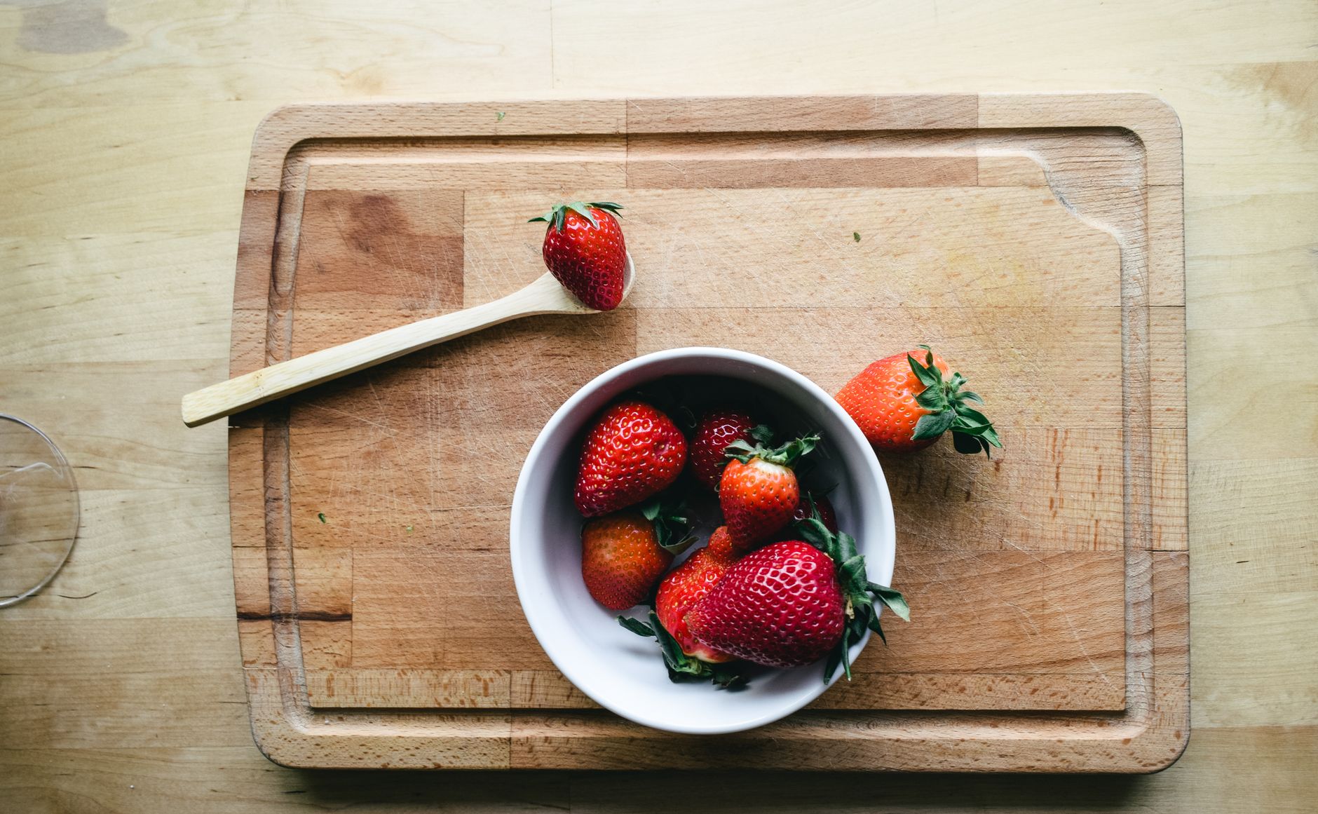 Pregnant hand resting on a soft wooden cutting board holding a small bowl of fresh berries, gentle natural light highlighting the fruit and the wrist