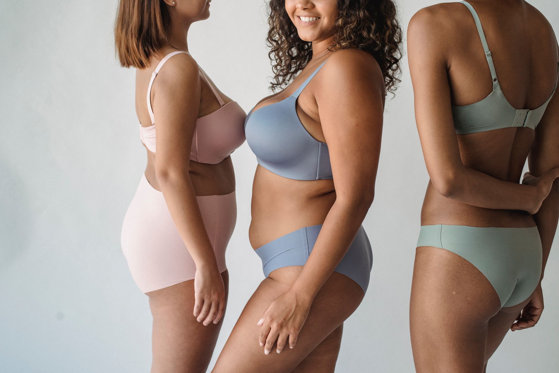 Four women of different body shapes standing side by side, all at 8 weeks pregnant, soft natural light
