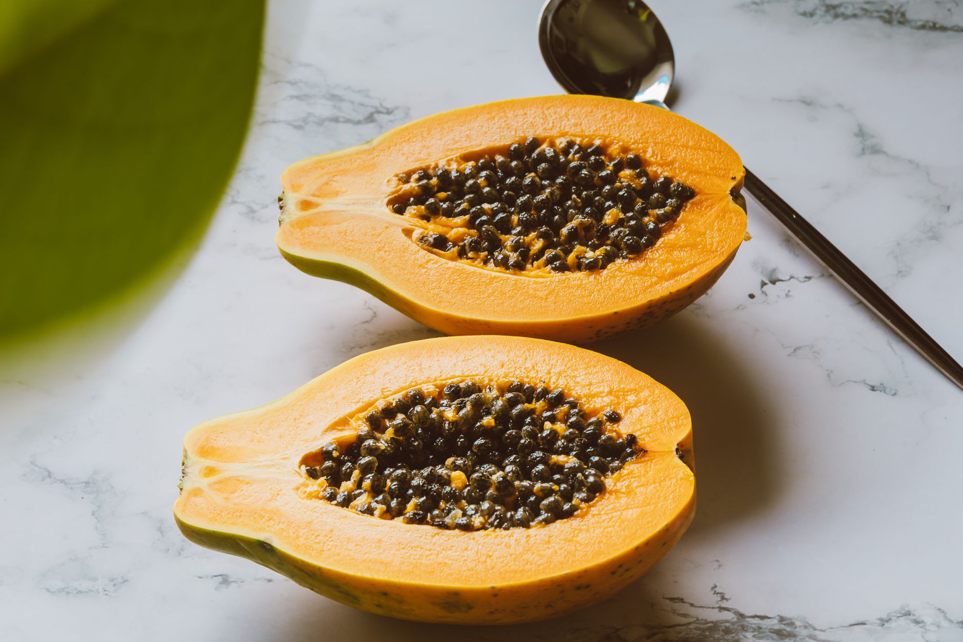 Close-up of a fresh, bright orange papaya sliced in half on a wooden cutting board, morning light highlighting the vibrant flesh