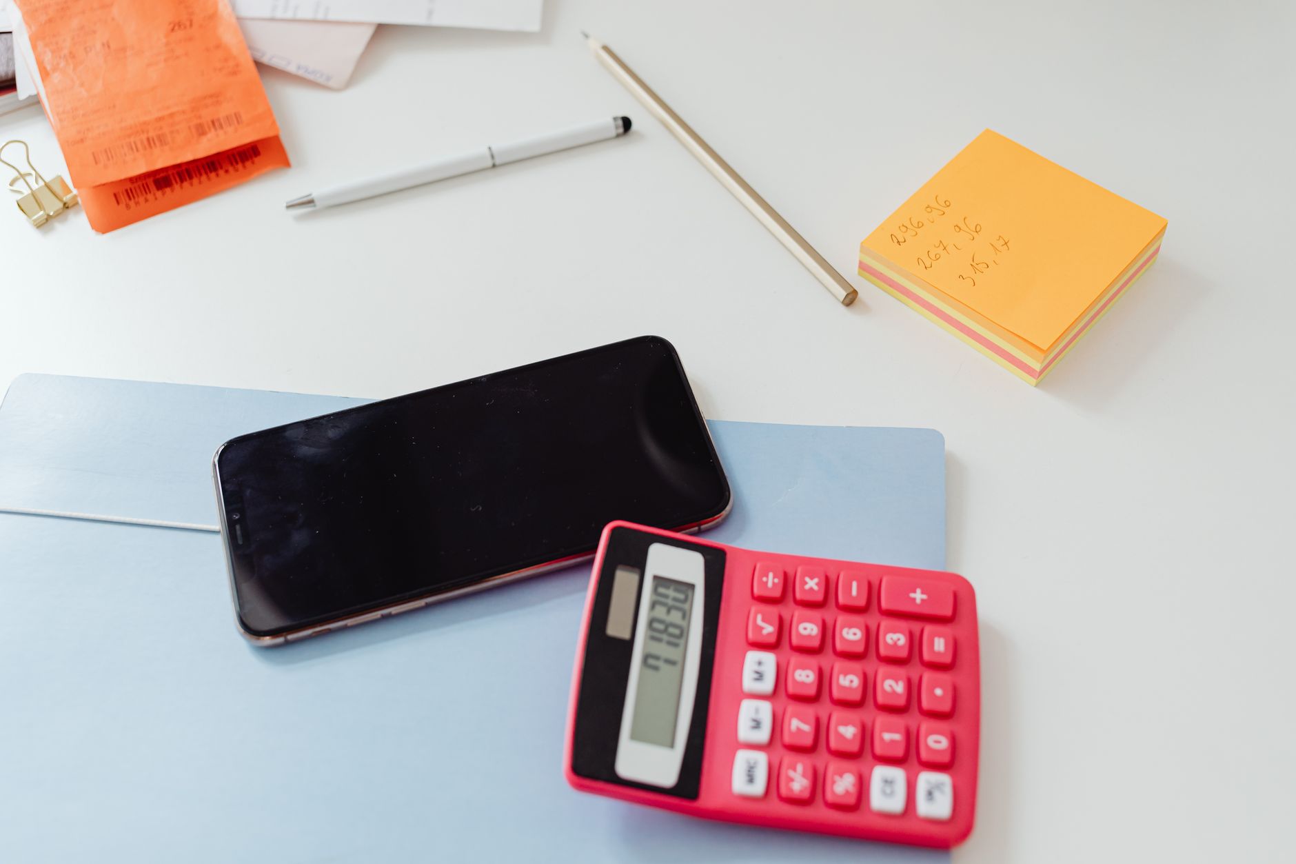 A calculator, bills, and a pen on a desk, symbolizing the financial planning involved when adding a newborn to health insurance.