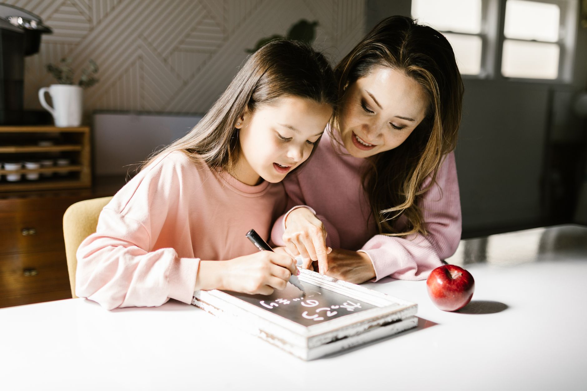 A parent and child sitting at a kitchen table with a whiteboard displaying daily routines, representing consistency and predictability