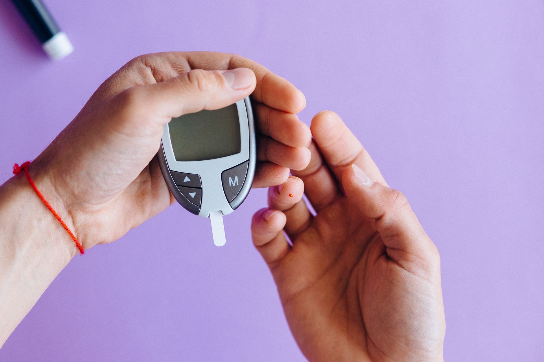 Close‑up of a glucose meter displaying a blood sugar reading, with a pregnant woman's hand holding the device, bright kitchen lighting