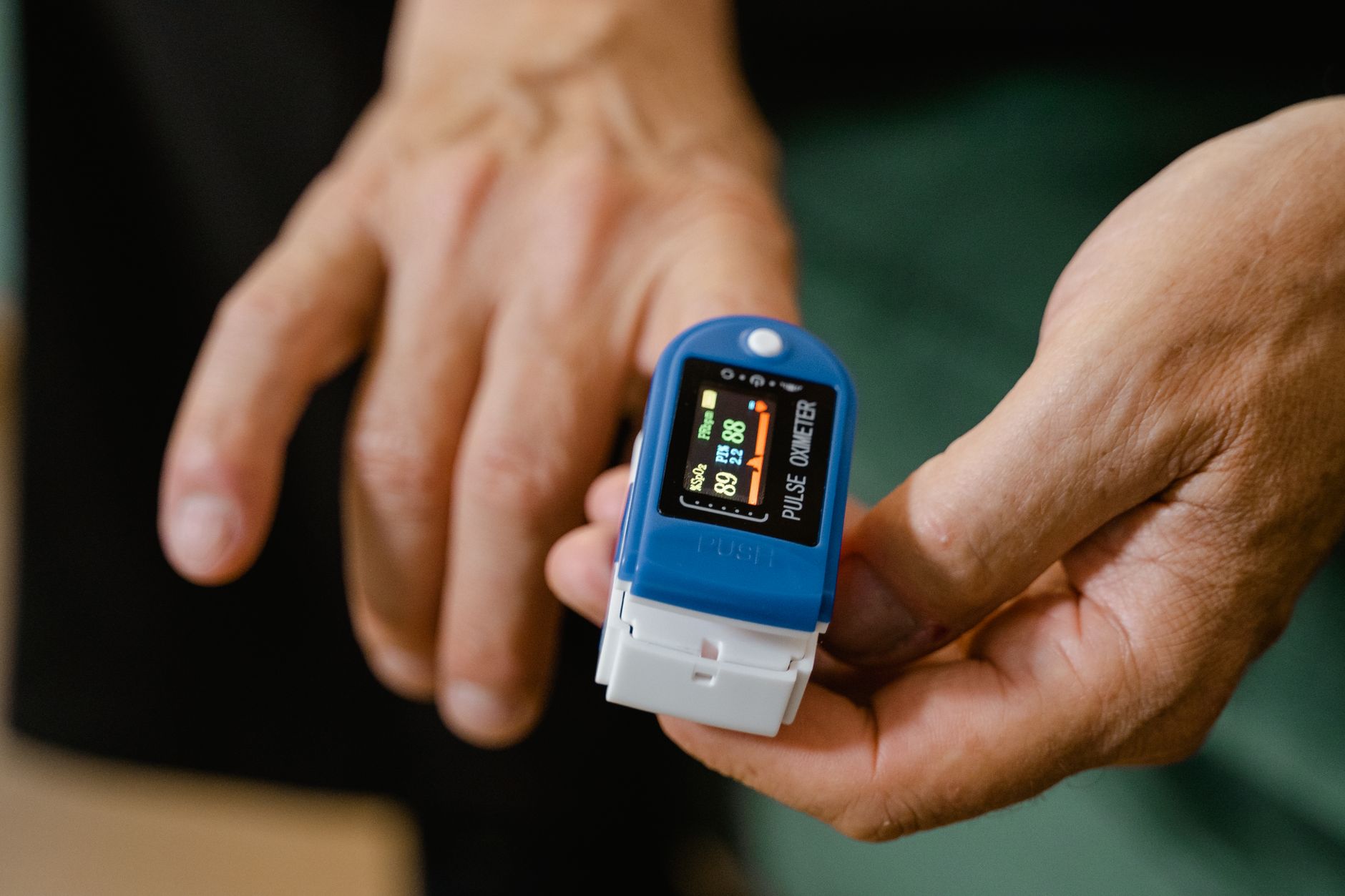 Close‑up of a handheld pulse oximeter reading 96% on a child's fingertip, with a soft pastel background