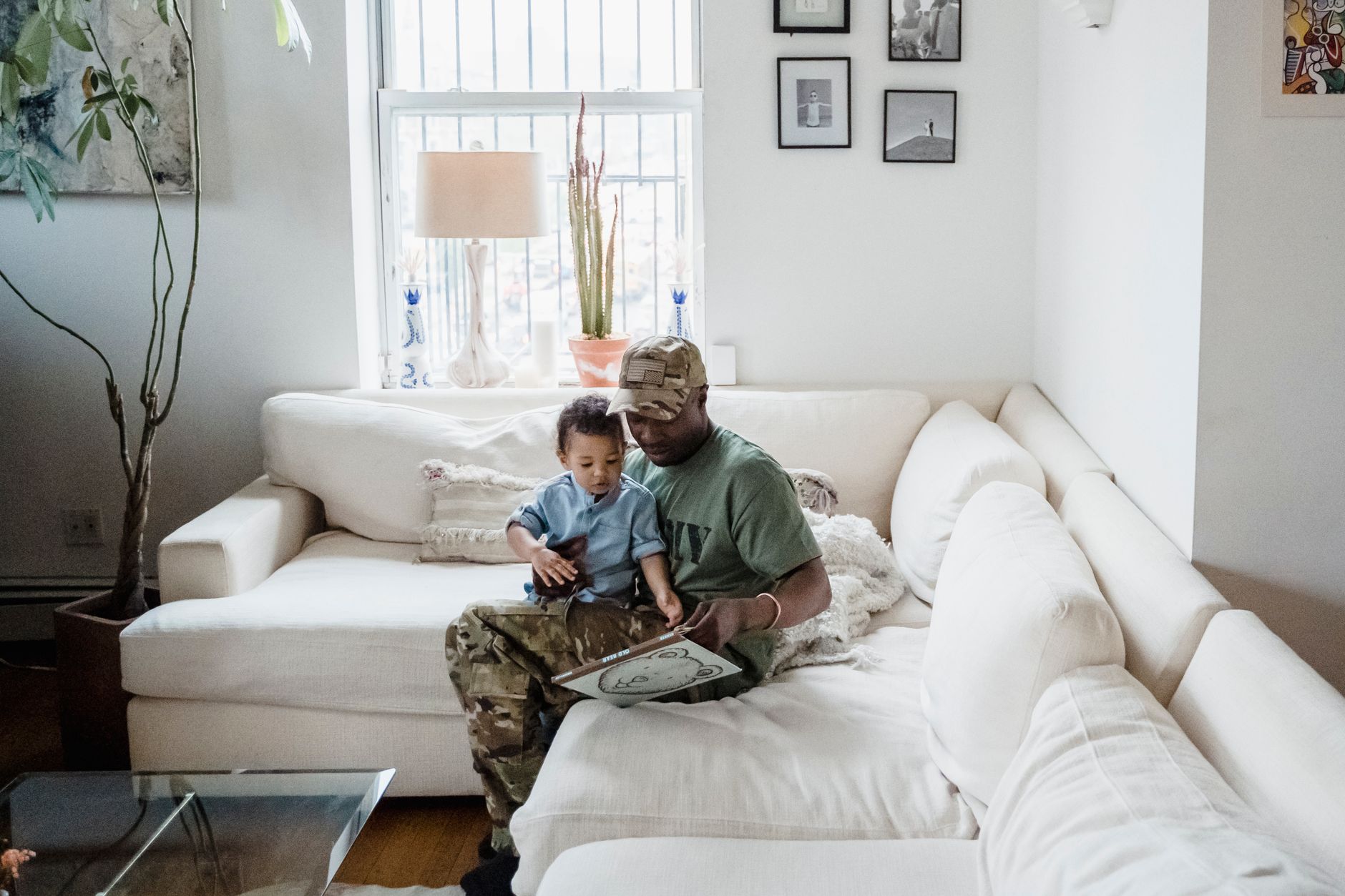 Parent and toddler sitting together on a couch, reading a book and smiling