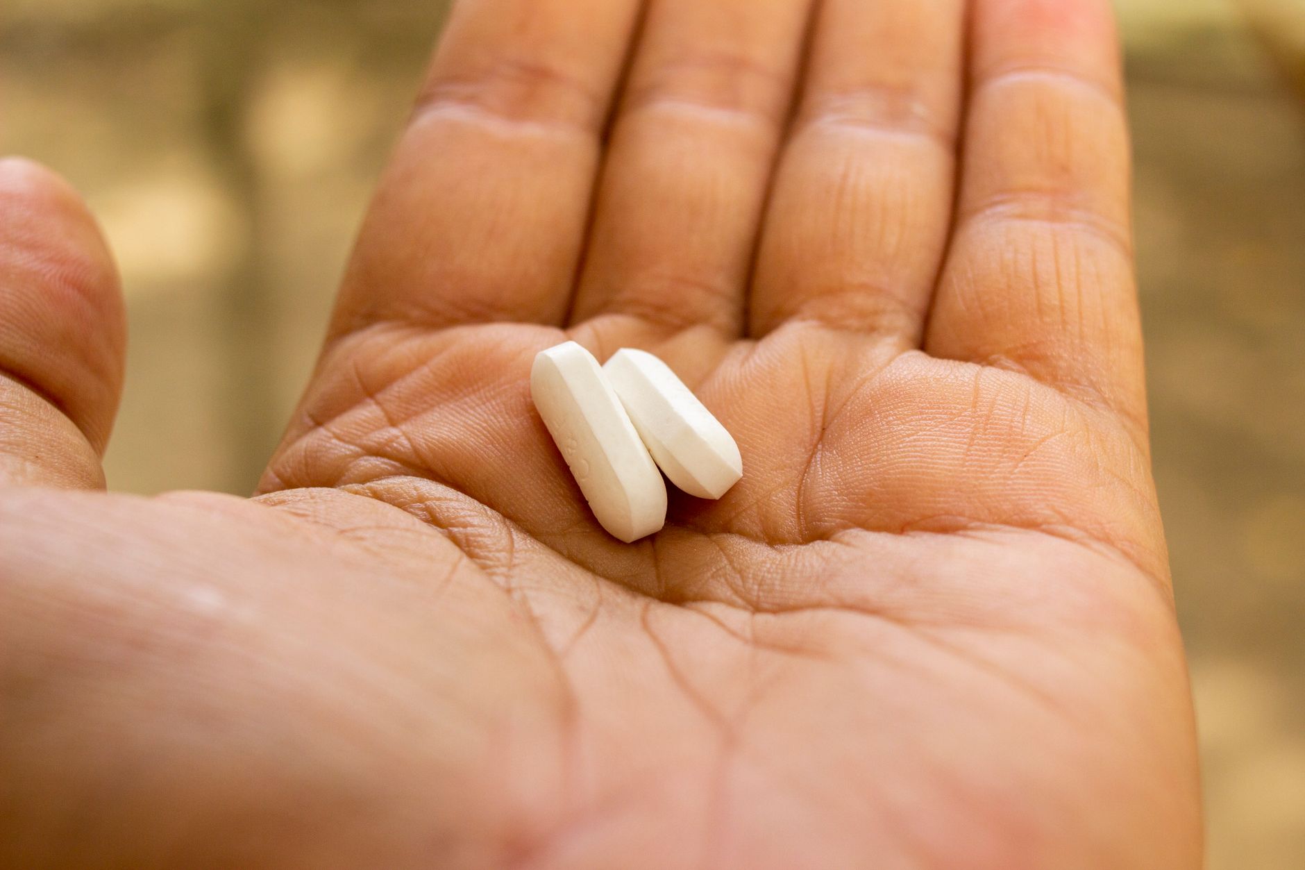 pregnant woman holding a baby aspirin tablet and a glass of water in soft lighting