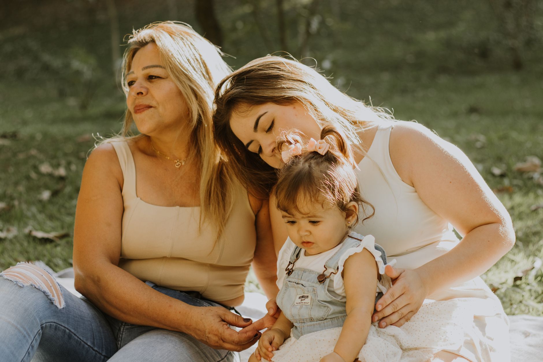 A supportive postpartum circle: a partner holding a cup of tea, a friend with a notebook, and a mother with a baby, sitting on a soft rug, natural light streaming through a window