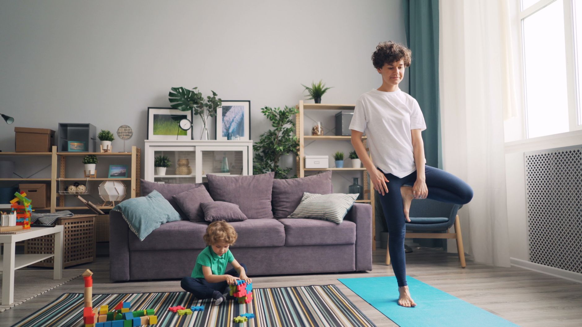 A gentle sunrise yoga session in a living room, a postpartum mother in comfortable clothing stretching on a yoga mat, soft natural light, plants in the background, calm atmosphere