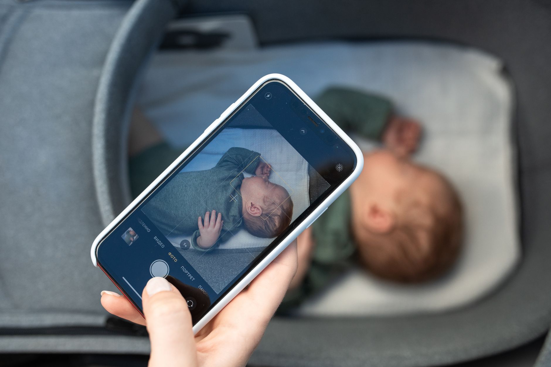 parent using a baby breathing monitor app on a smartphone while holding a sleeping infant in a softly lit nursery