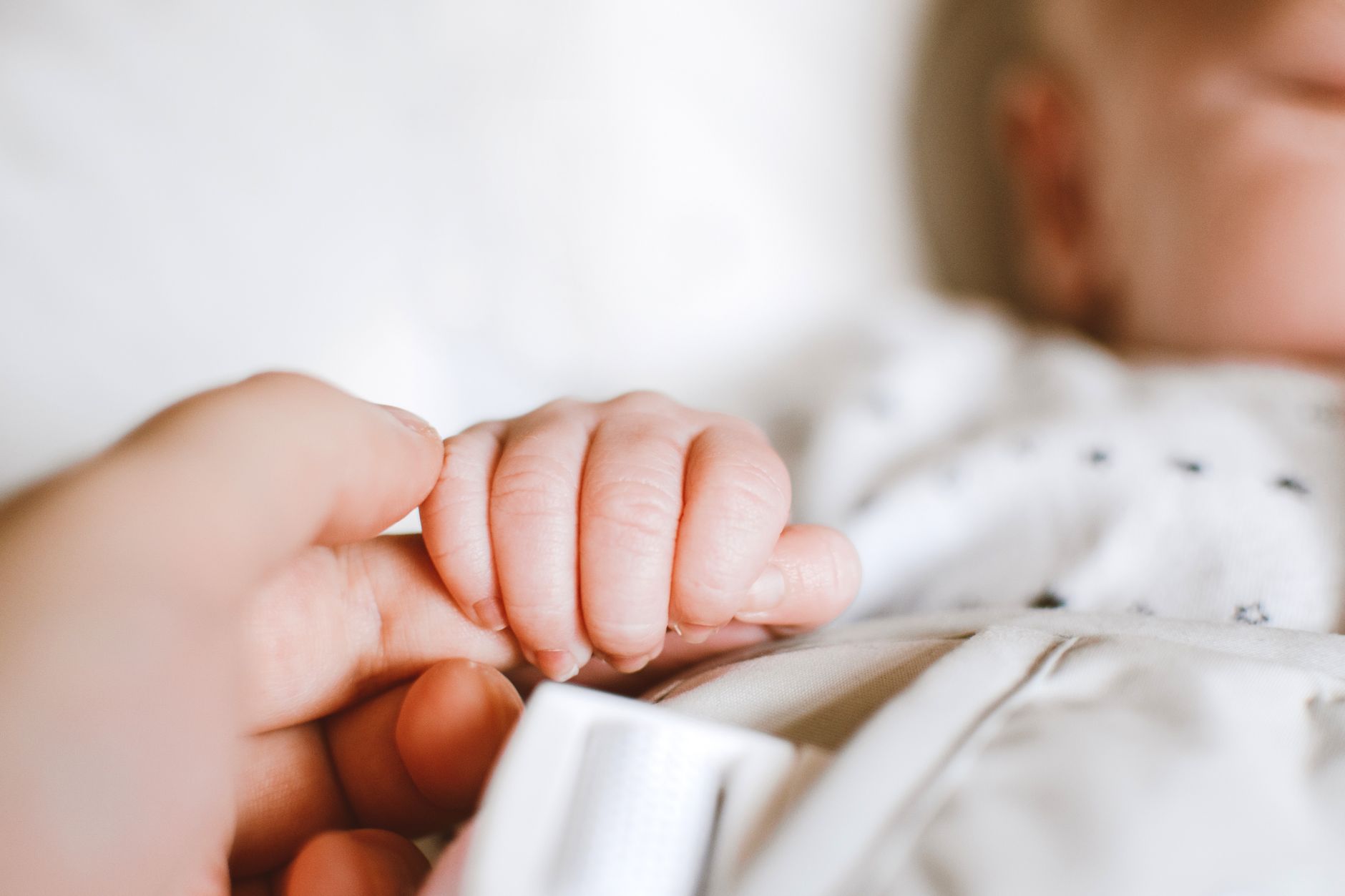A close-up of a baby's hand gently grasping an adult's finger, symbolizing care and reassurance.