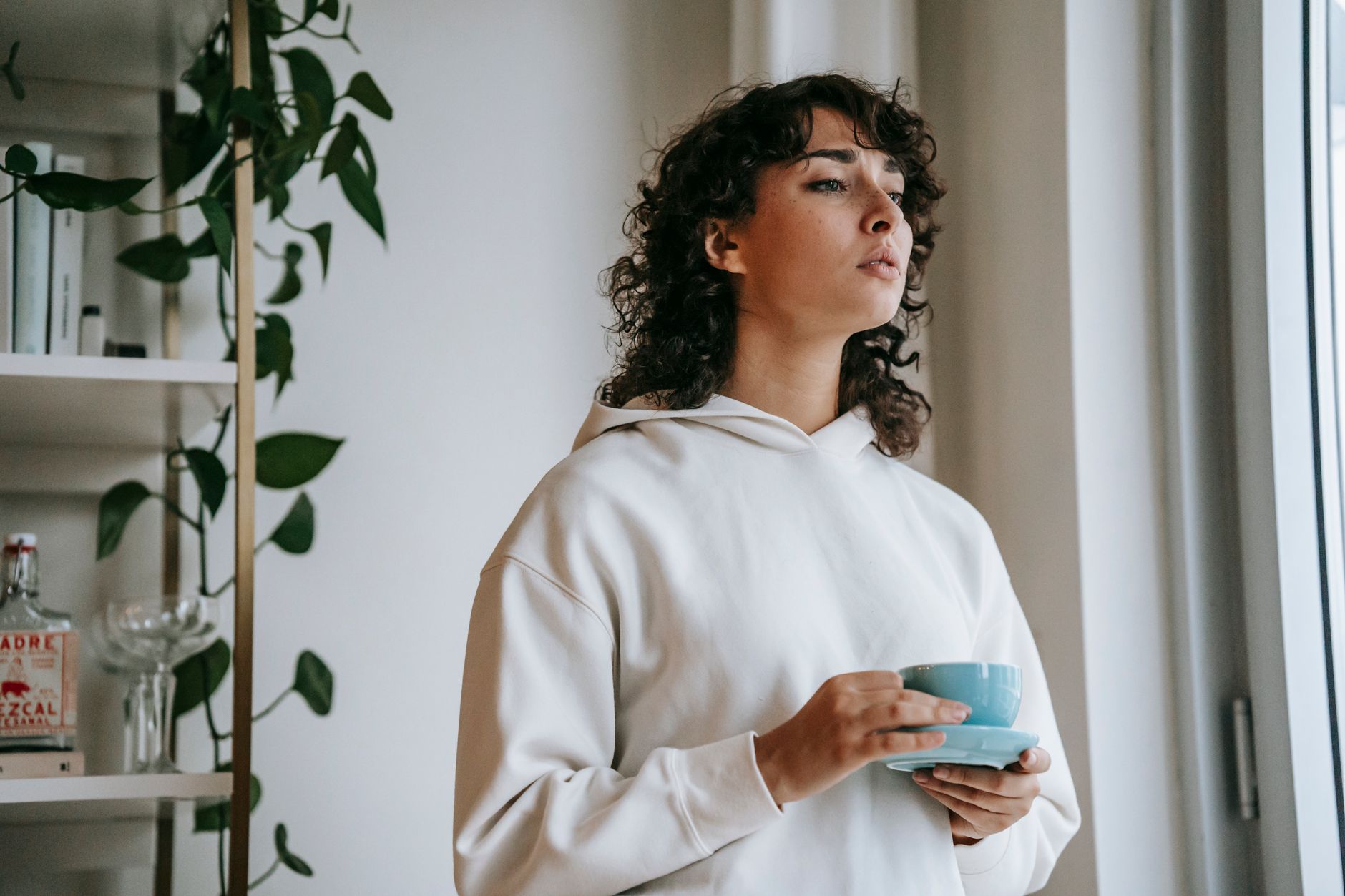 A calm woman sitting on a sofa, holding a warm mug, with soft focus on the background, conveying comfort and reflection.