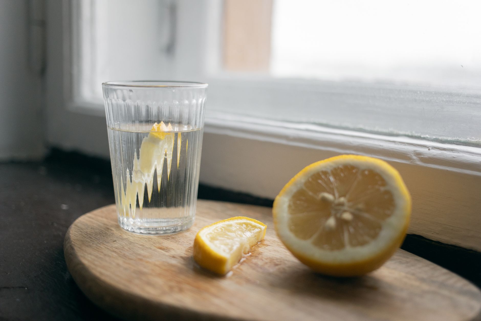 A pregnant woman taking a sip of water with a lemon slice in a bright kitchen