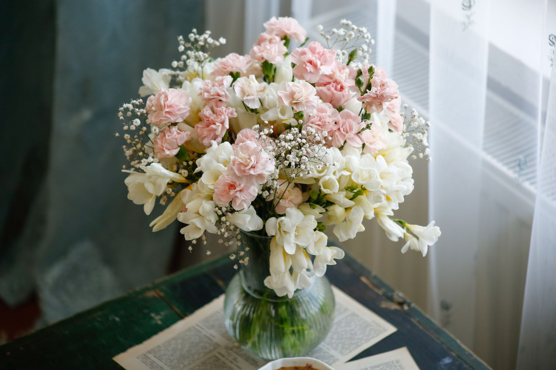 A pastel baby certificate printed on cream cardstock, displayed on a wooden desk with a small vase of flowers and a baby handprint