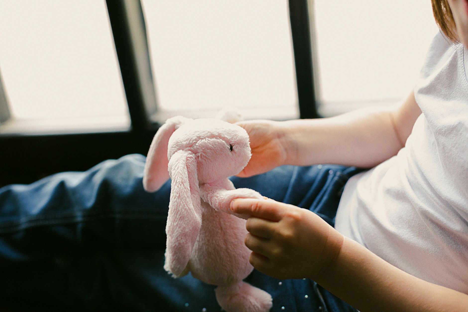 A one‑year‑old toddler taking a tentative step on a soft rug, mother’s hand nearby for support, bright living room with toys