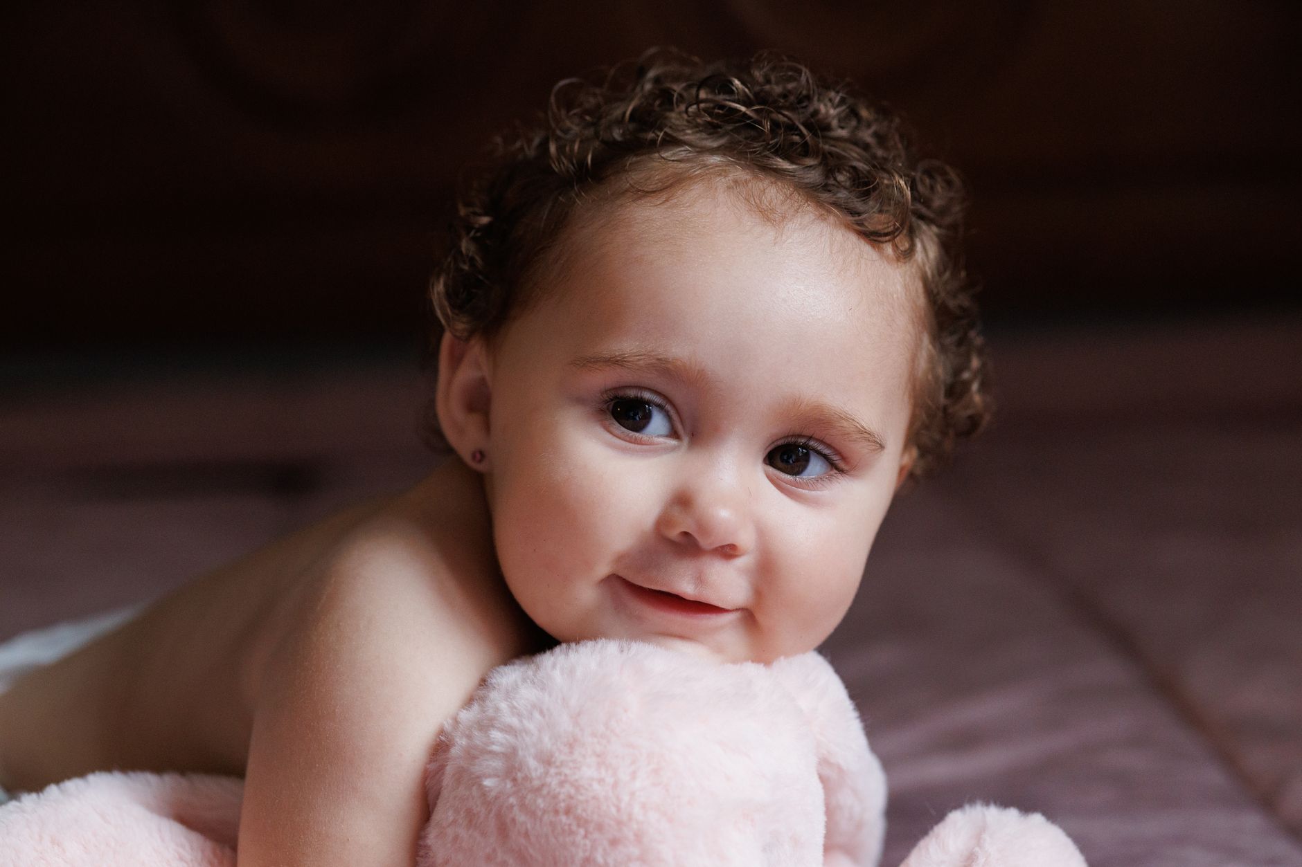 A smiling parent holding a five‑month‑old baby on a soft rug, natural window light, warm tones, with plush toys scattered nearby