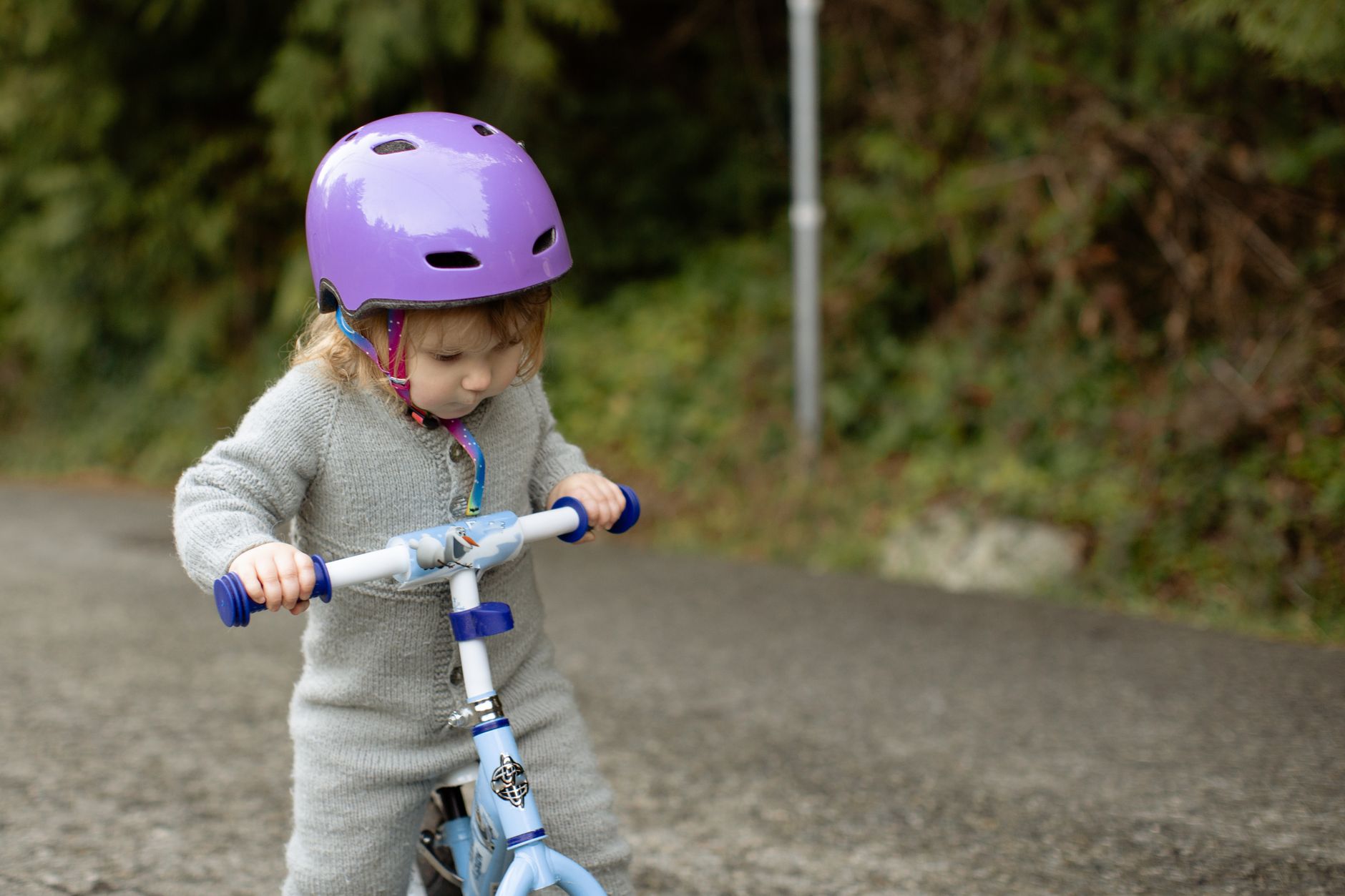Toddler wearing a helmet while riding a balance bike in a driveway