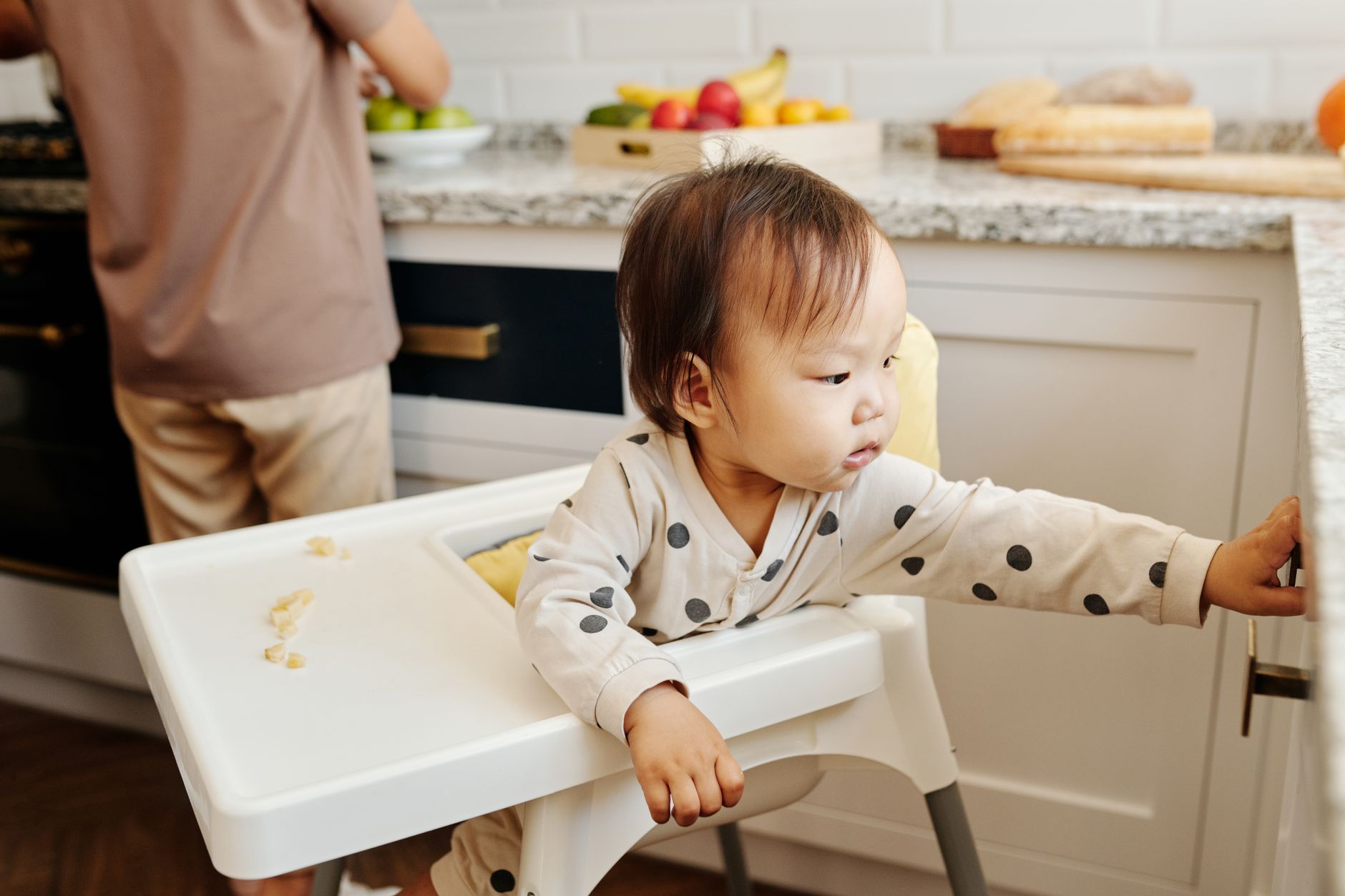 Parent cleaning food off the floor while baby watches from high chair