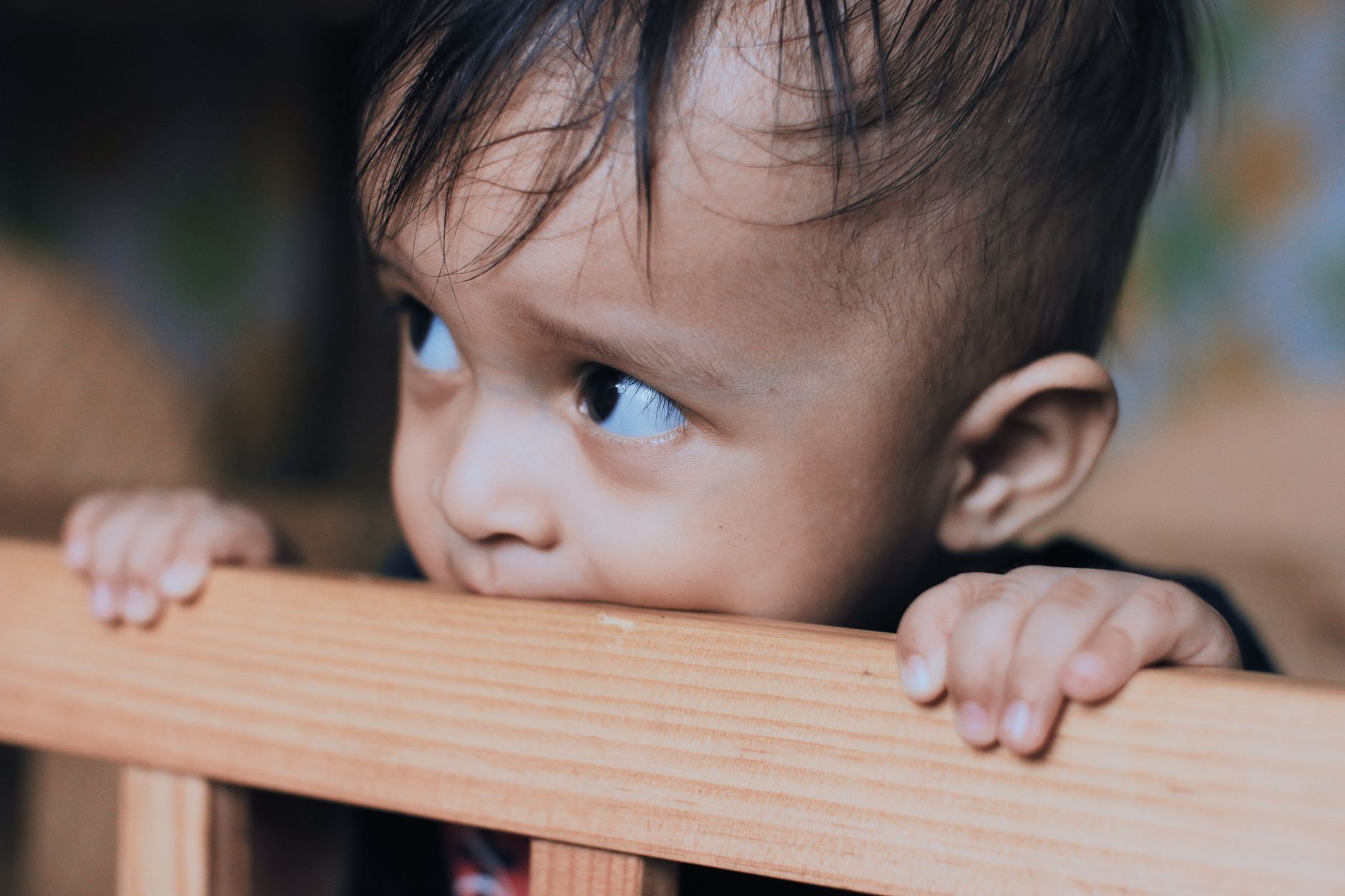 Infant sleepy eyes with a soft blanket draped over a wooden crib, warm morning light streaming through a window