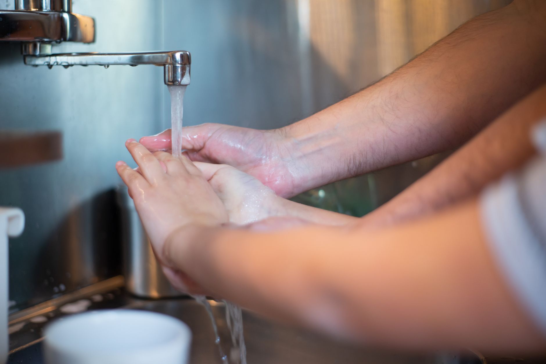 A parent gently washing a baby's hands with soap and water, soft focus on tiny hands and gentle bubbles, warm lighting
