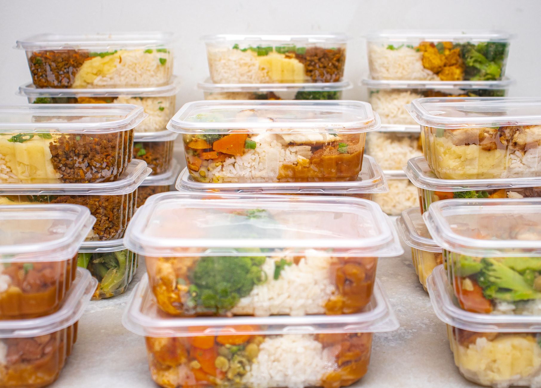 A variety of batch-cooked meals neatly stored in clear, labeled glass containers in a refrigerator, ready for the week.