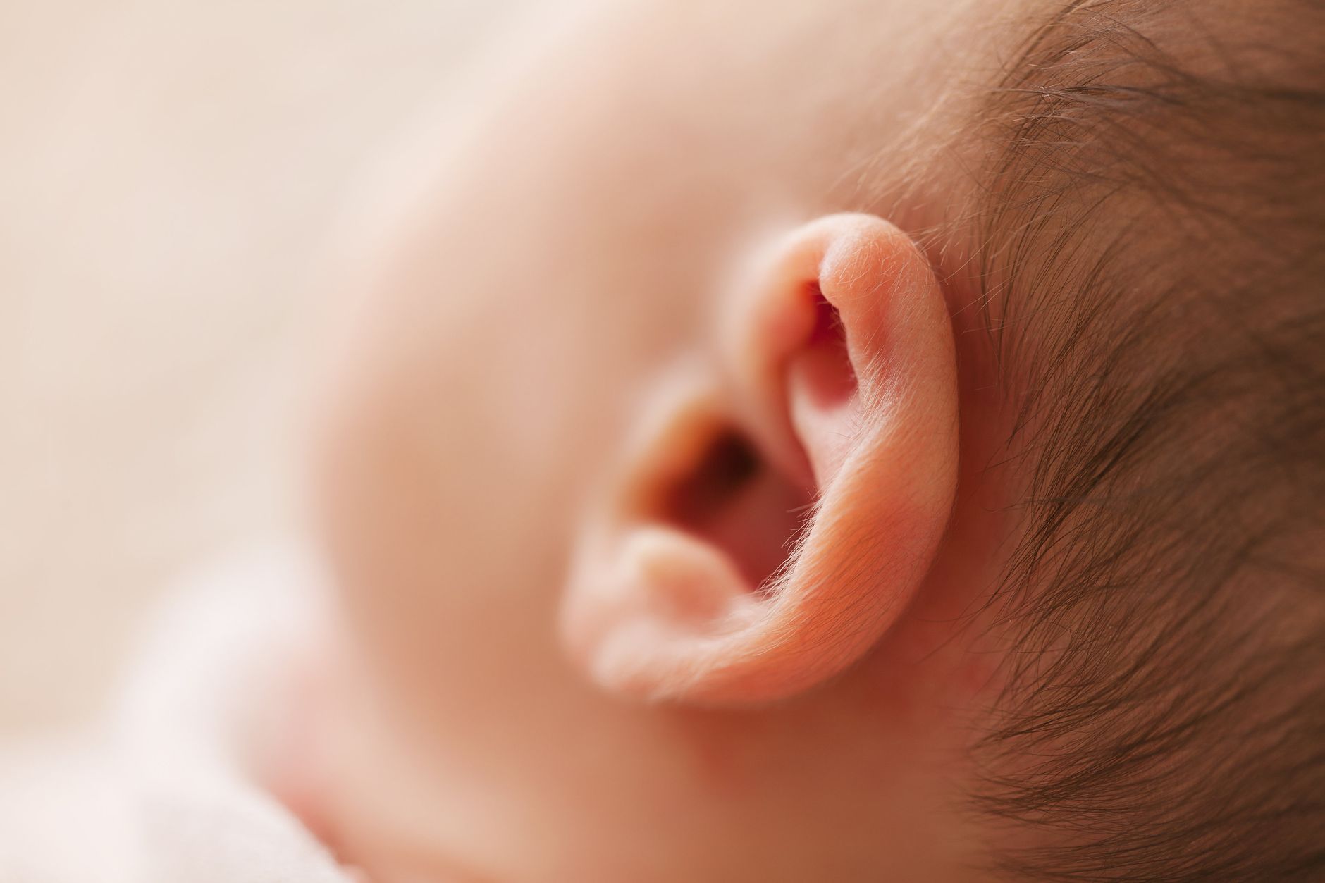 close‑up of a baby’s earlobe with a tiny 14‑karat gold stud, soft lighting highlighting the gentle shine and the surrounding skin, illustrating a hypoallergenic earring choice for infants