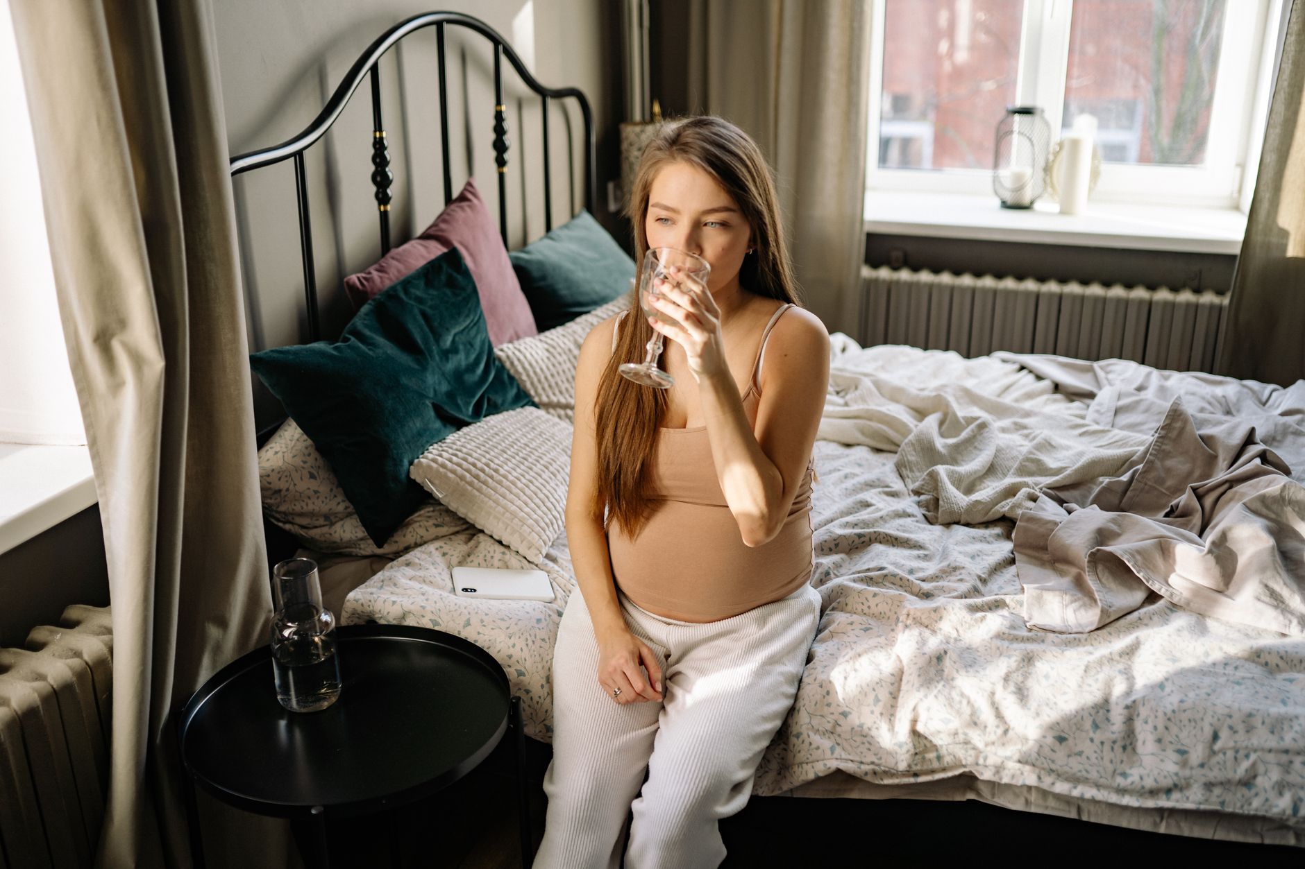 A pregnant woman with a serene expression, holding a glass of water, symbolizing reflection and hydration during pregnancy.